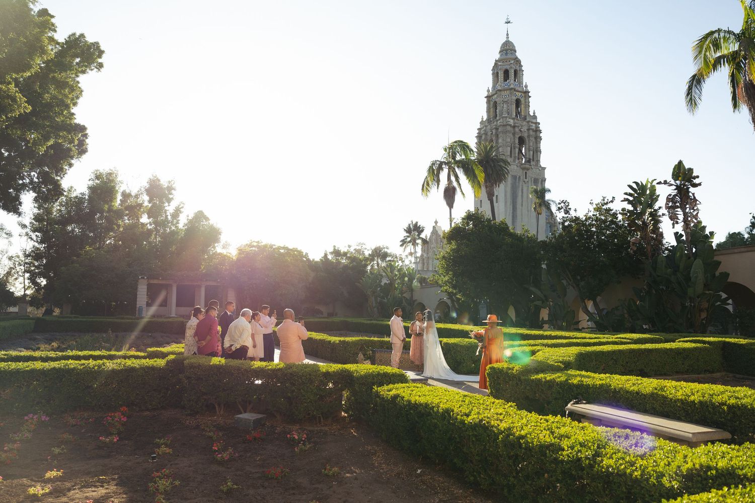 Outdoor wedding ceremony in a garden maze at Balboa Park with California Tower in background during golden hour.