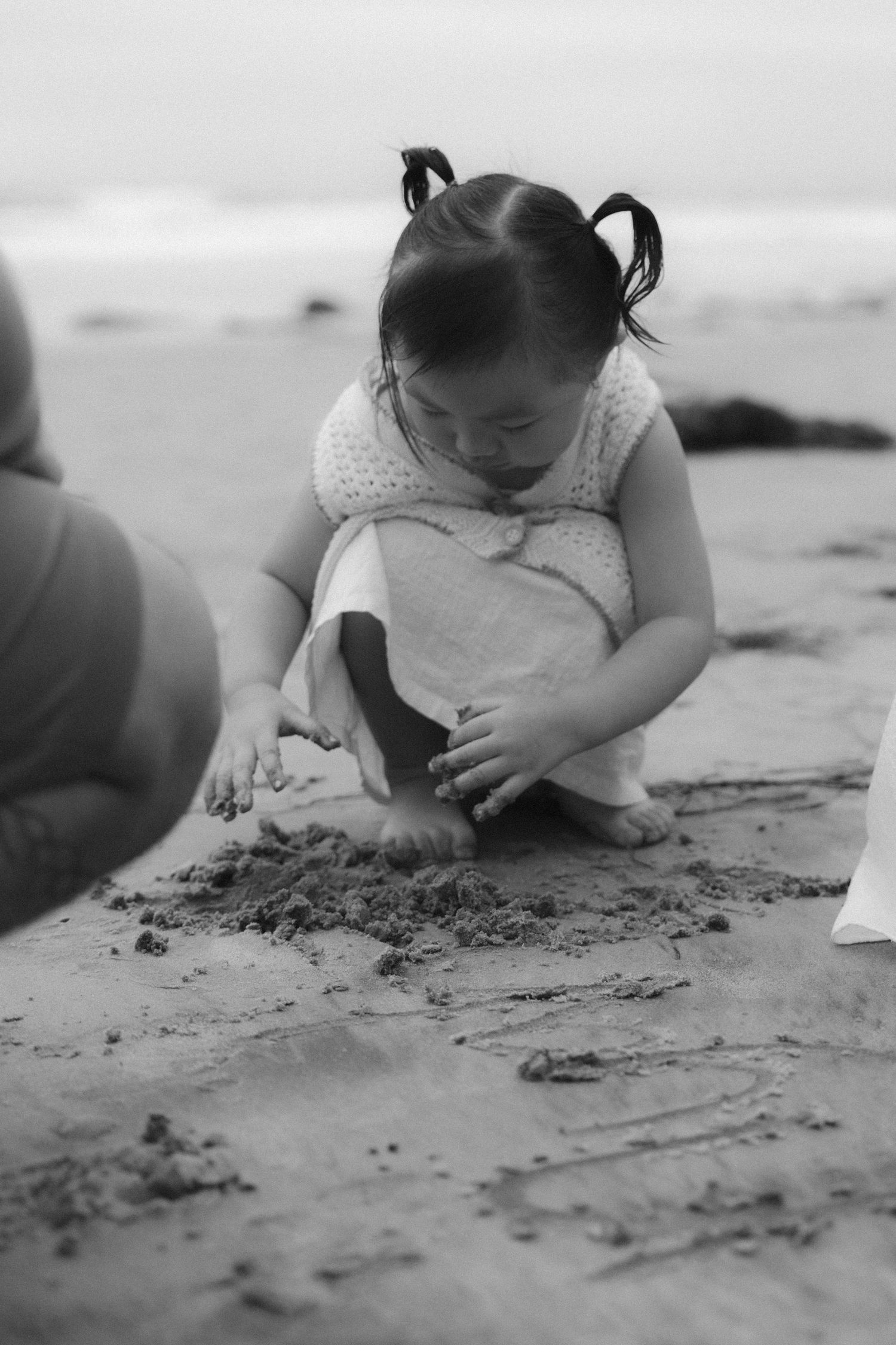 A black and white image sequence shows someone writing in the sand on a beach, capturing the process in detail.