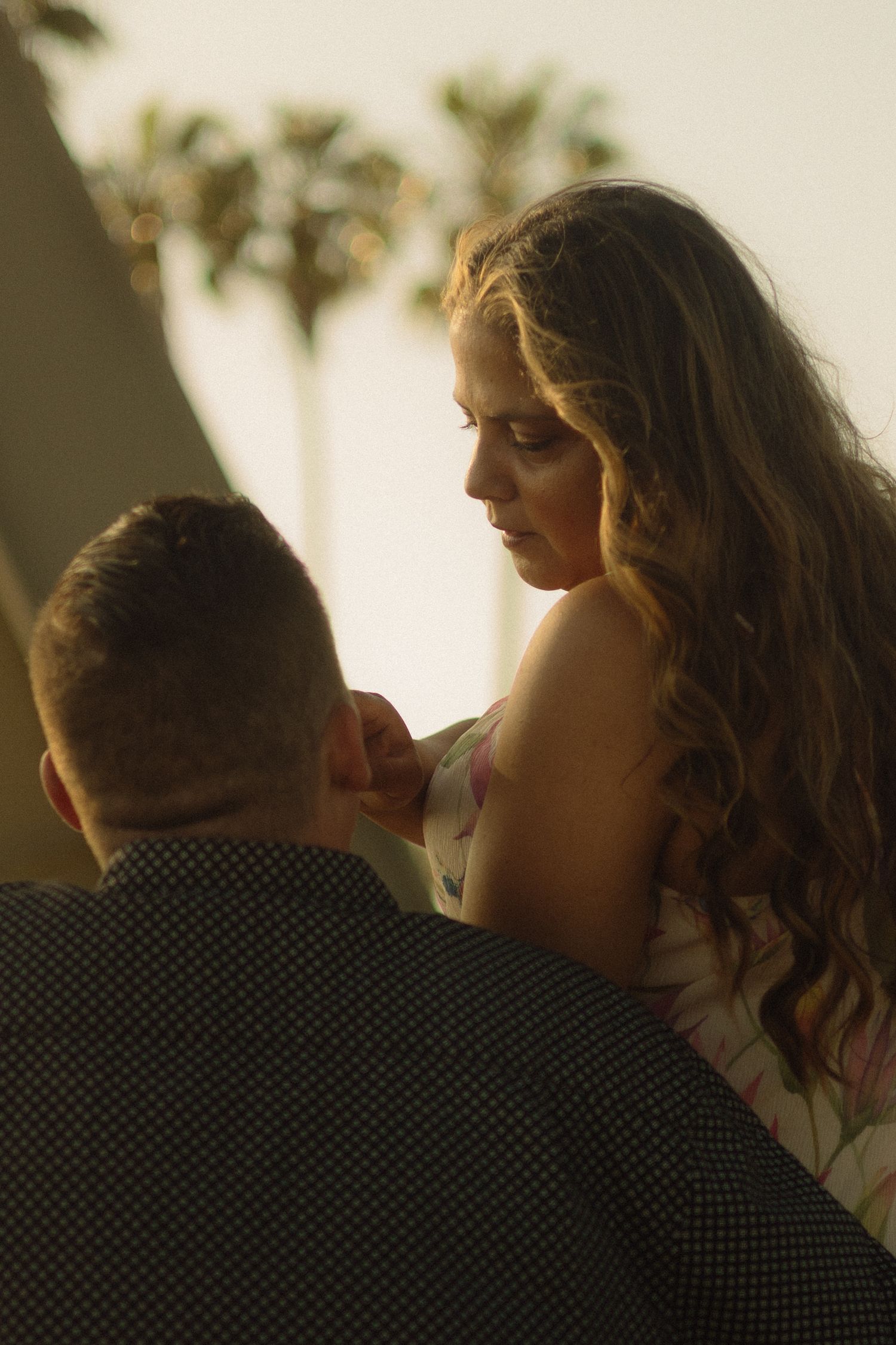 Intimate portrait of a couple in warm golden light with palm trees silhouetted in the background.