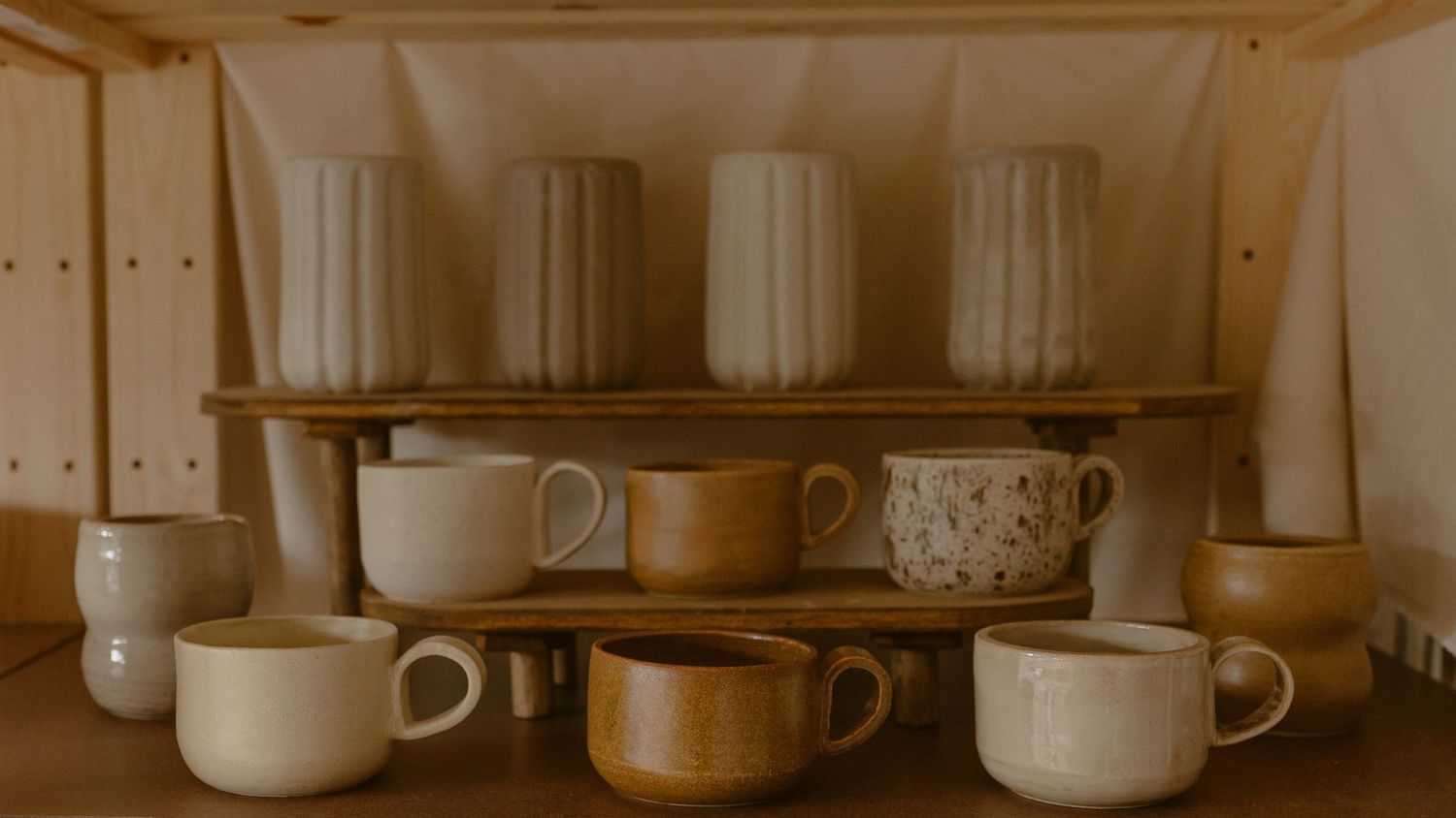Collection of white ceramic cups and mugs displayed on wooden shelving.