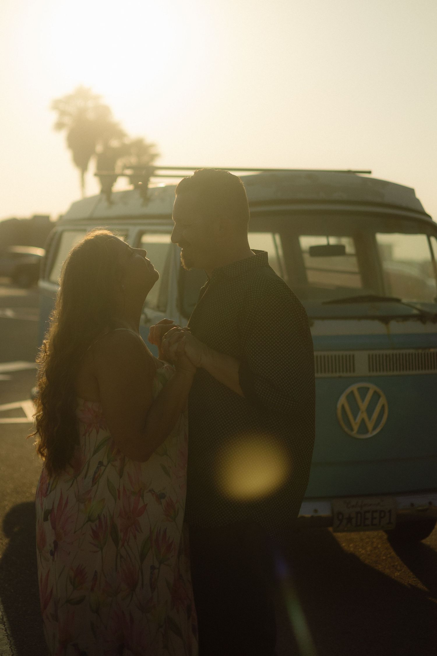 Silhouetted couple stands beside a classic Volkswagen van during golden hour sunset.