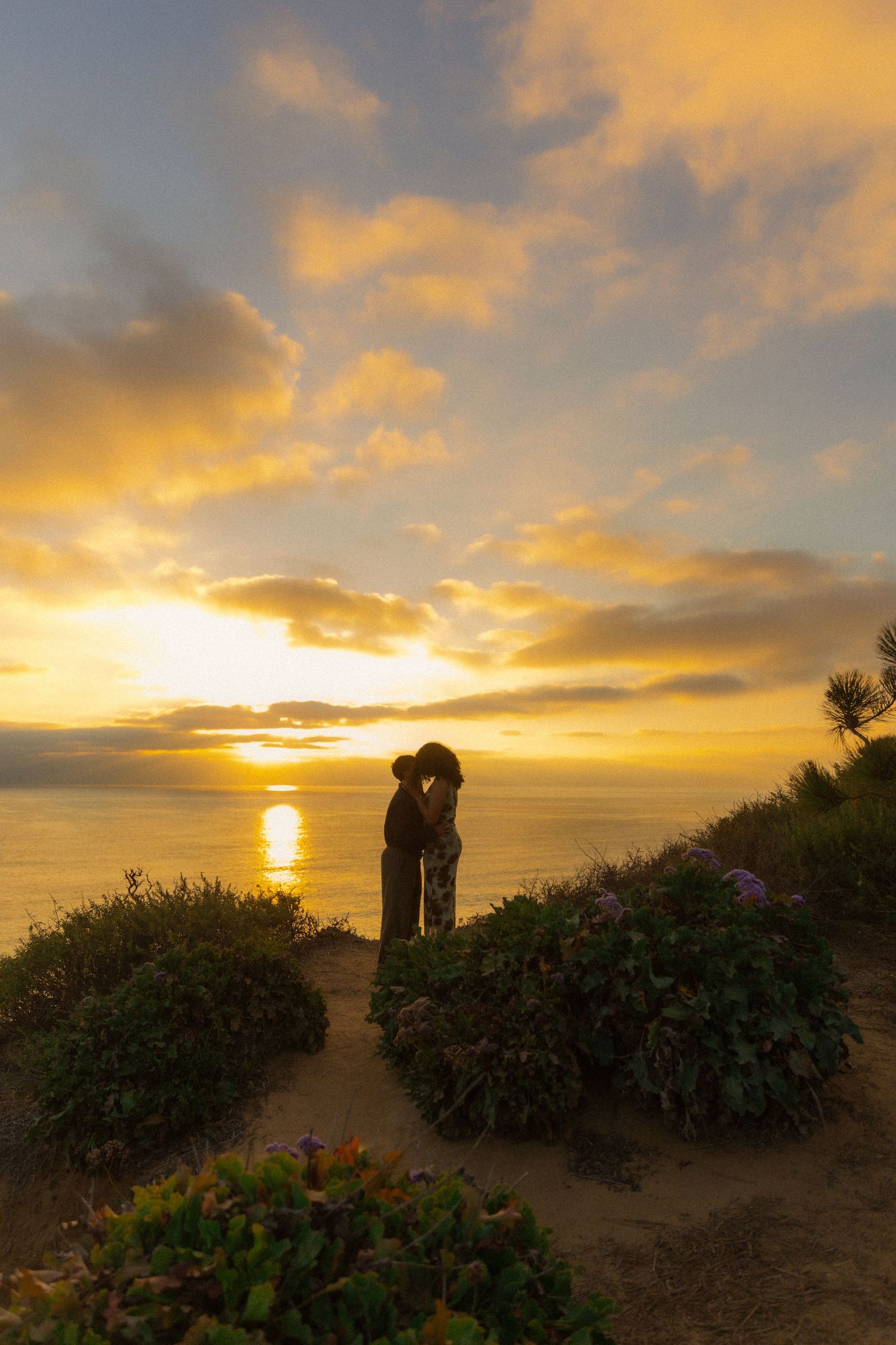 Stunning golden sunset over coastal cliffs with silhouettes of people against the dramatic orange and yellow sky.