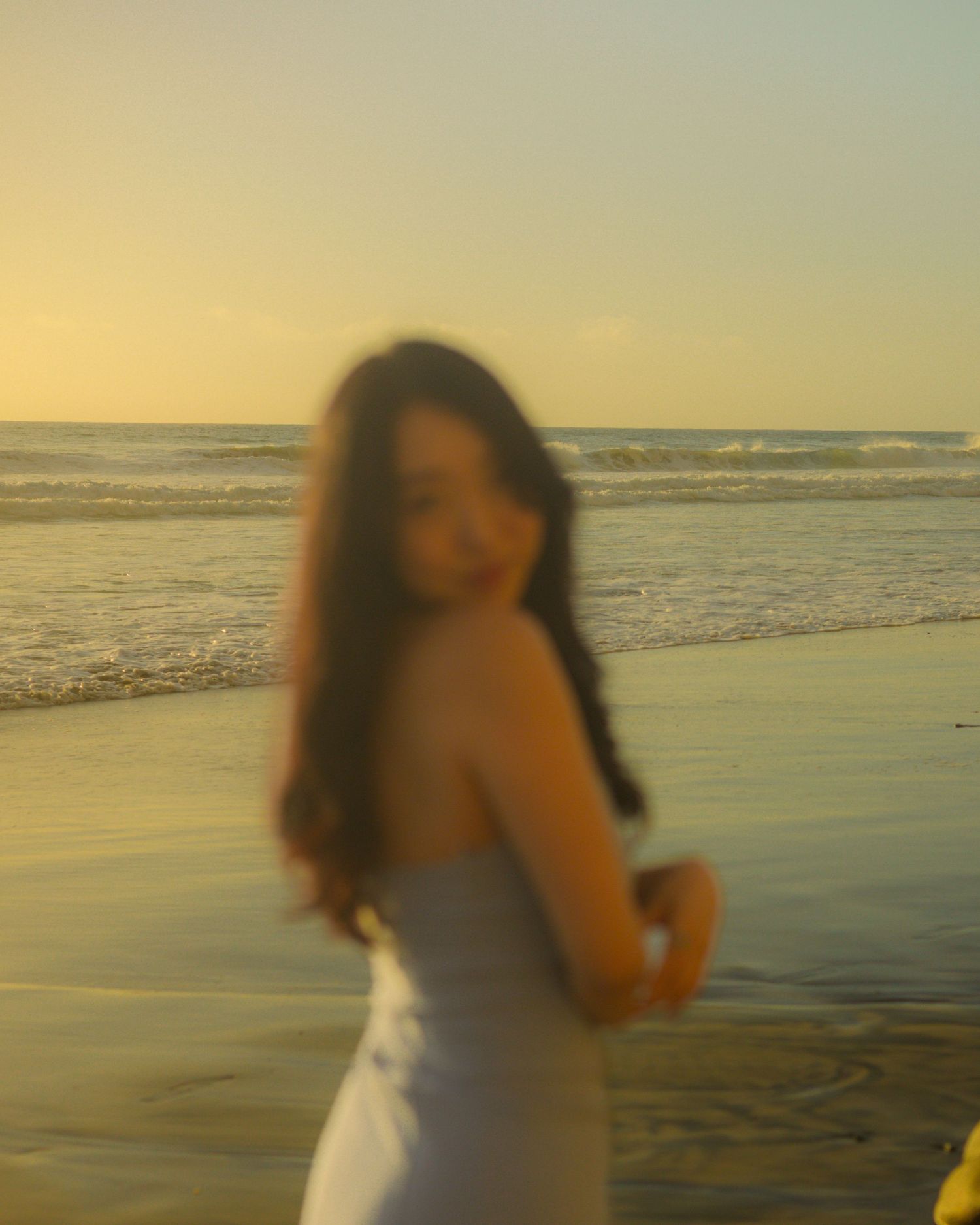 Woman in white dress twirling at sunset on a golden beach.