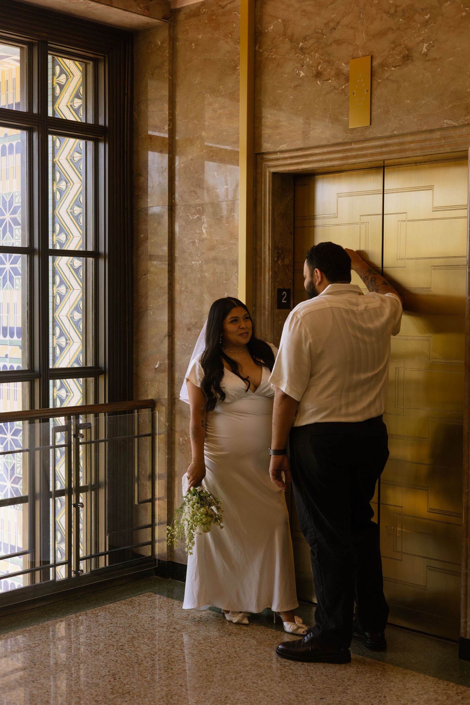 People stand near large windows in a dimly lit historic building interior with stone walls.