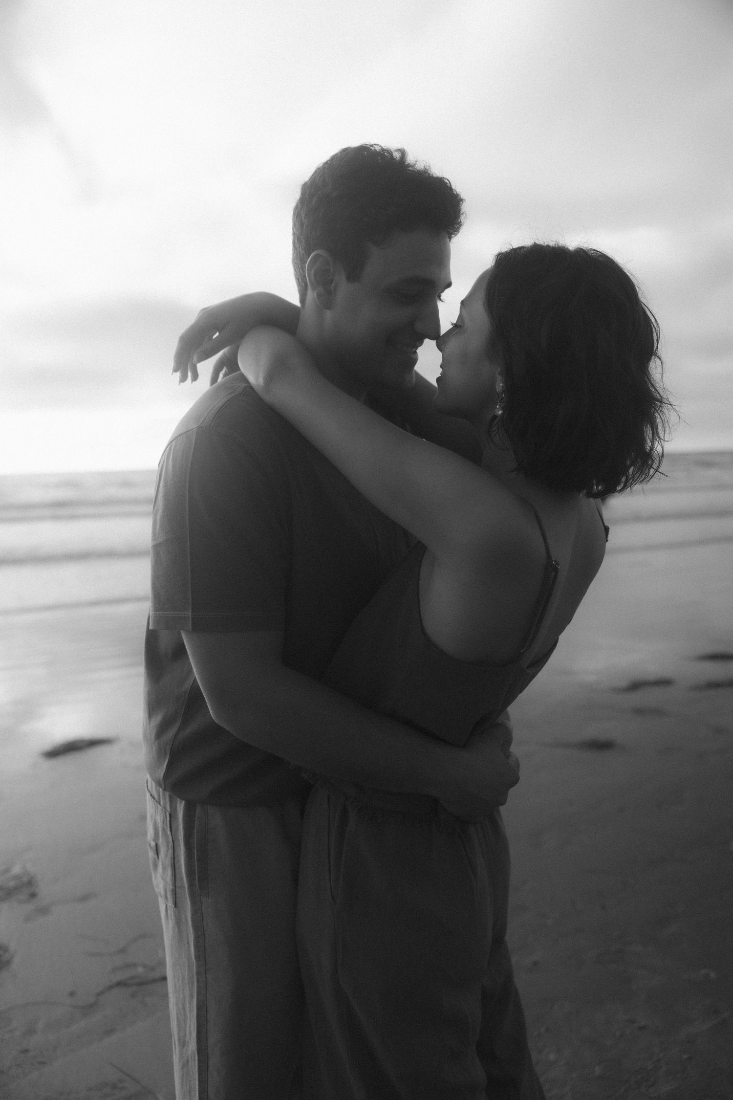 A romantic couple embraces on a misty beach in black and white photography.