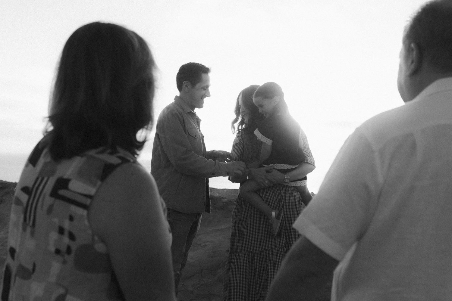 A black and white photograph shows people gathered outdoors in casual conversation at dusk.