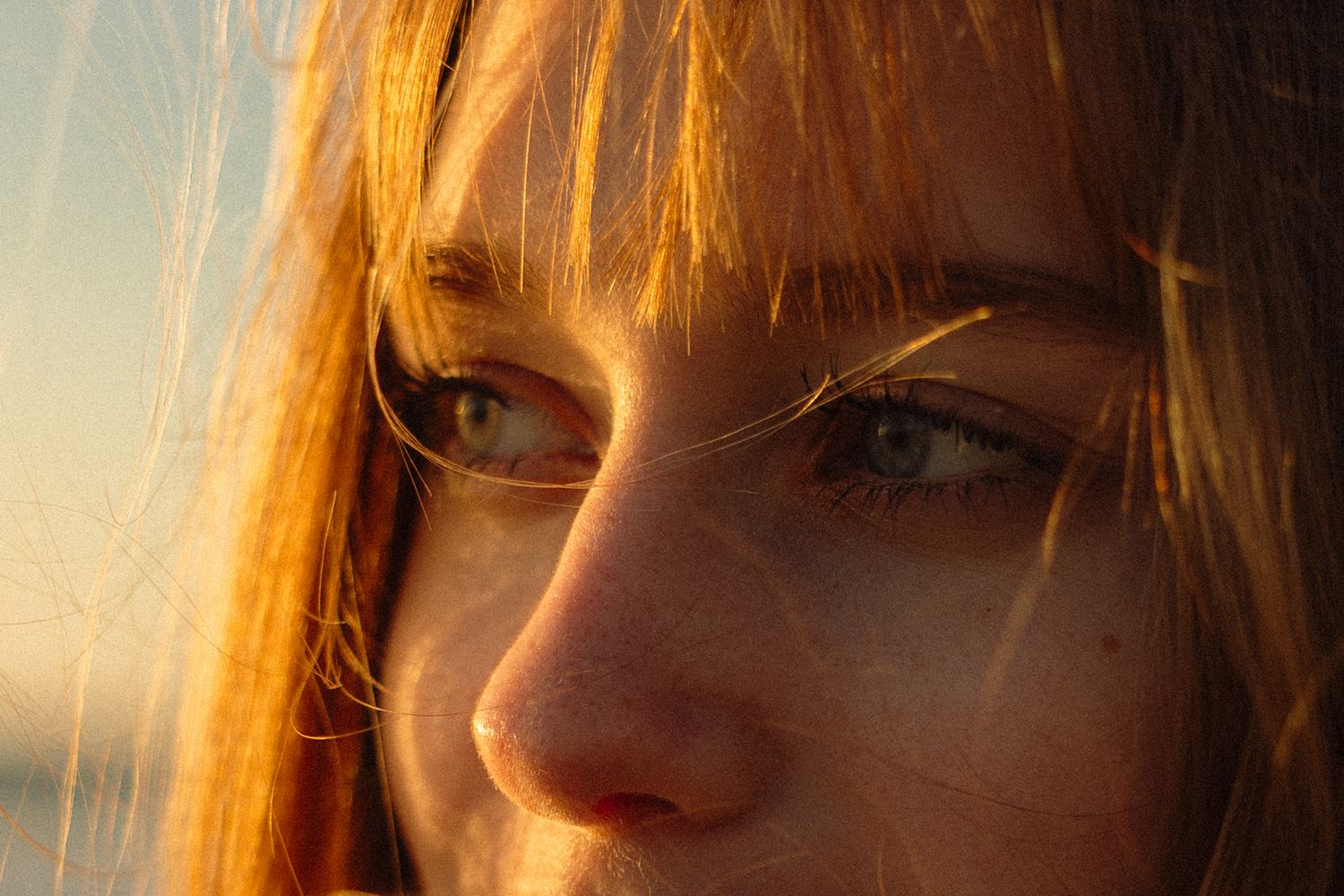 Close-up portrait of a young woman with green eyes and red hair in warm golden sunset light.