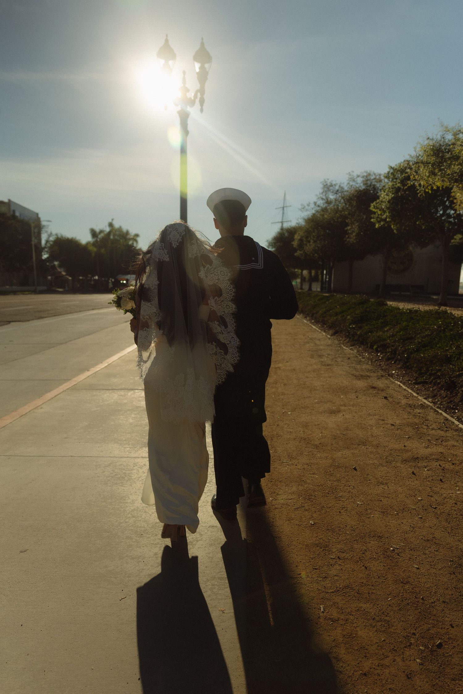 Two silhouetted figures walk together on a path at sunset with bright sunlight glinting off a lamp post ahead.