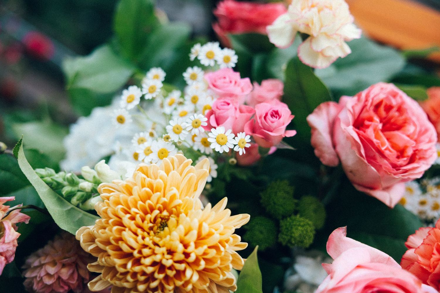 A vibrant bouquet featuring pink roses, yellow chrysanthemums, white daisies, and green accents in full bloom.