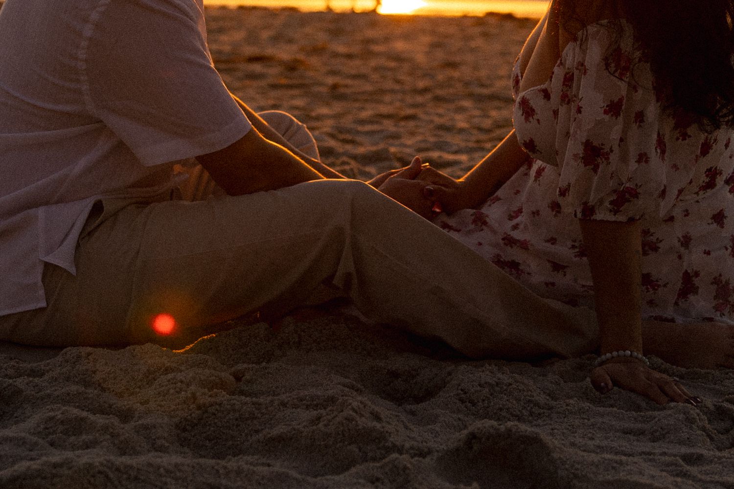 Person sitting on sandy beach at sunset with golden light creating silhouette against orange sky.