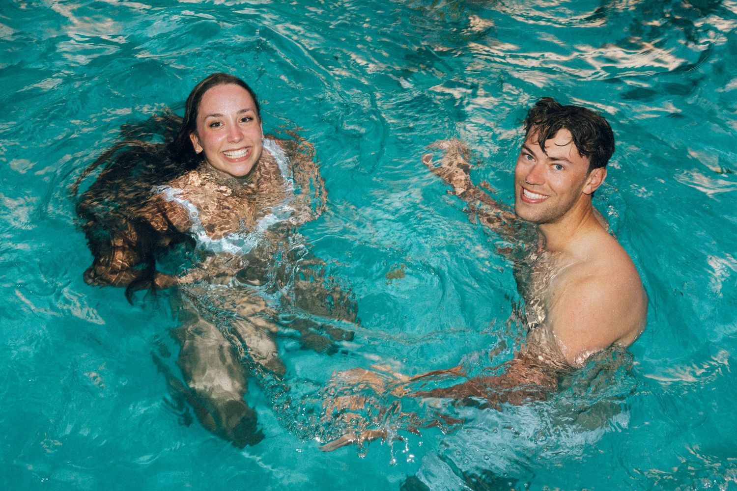 Two smiling people swimming together in a clear turquoise pool, enjoying a fun swim session.