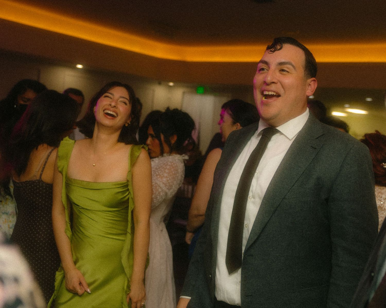 Wedding party celebrating with laughter and dancing in a dimly lit reception venue.