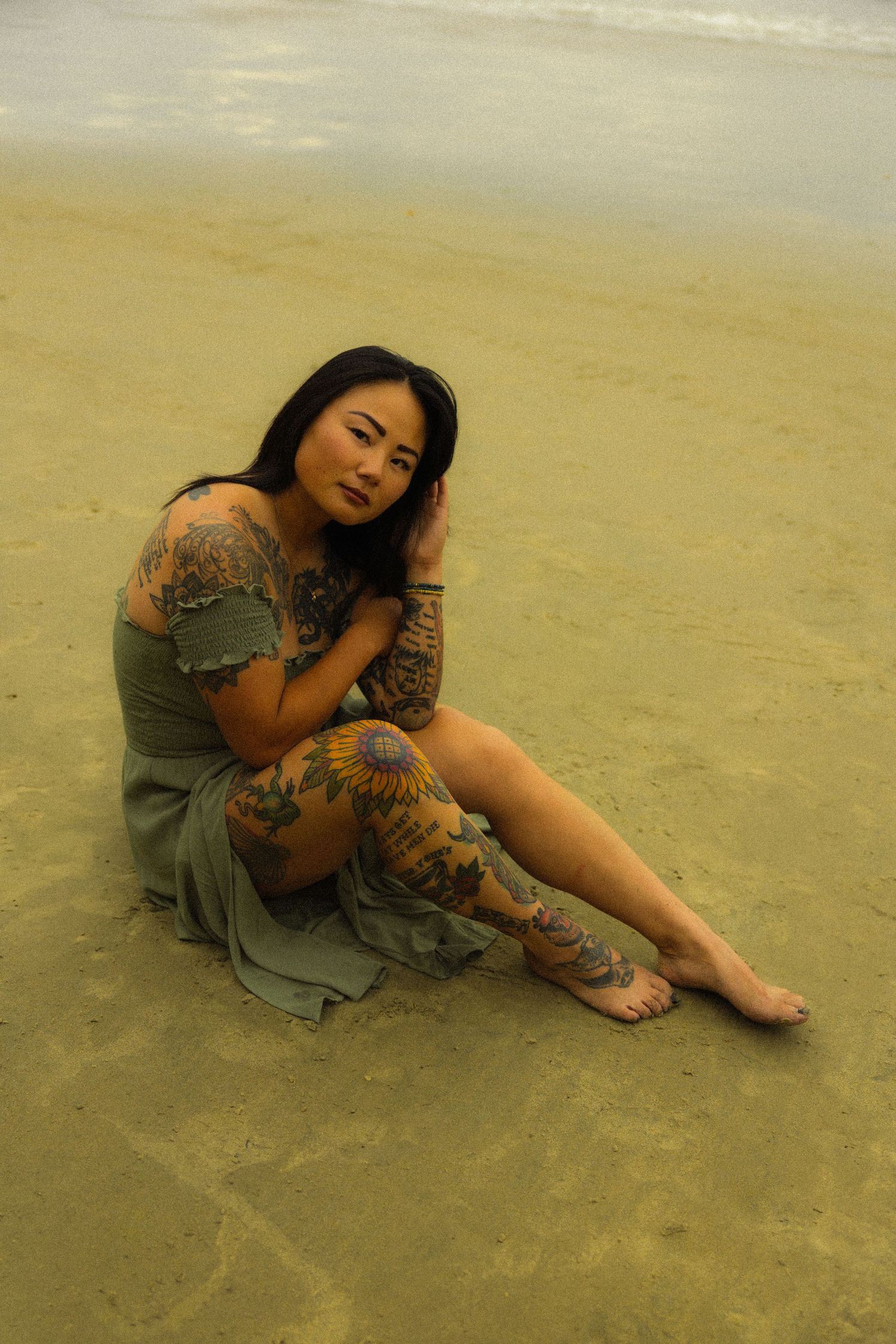 A woman in a grey dress sits on a sandy beach in a series of artistic poses against a neutral beige background.