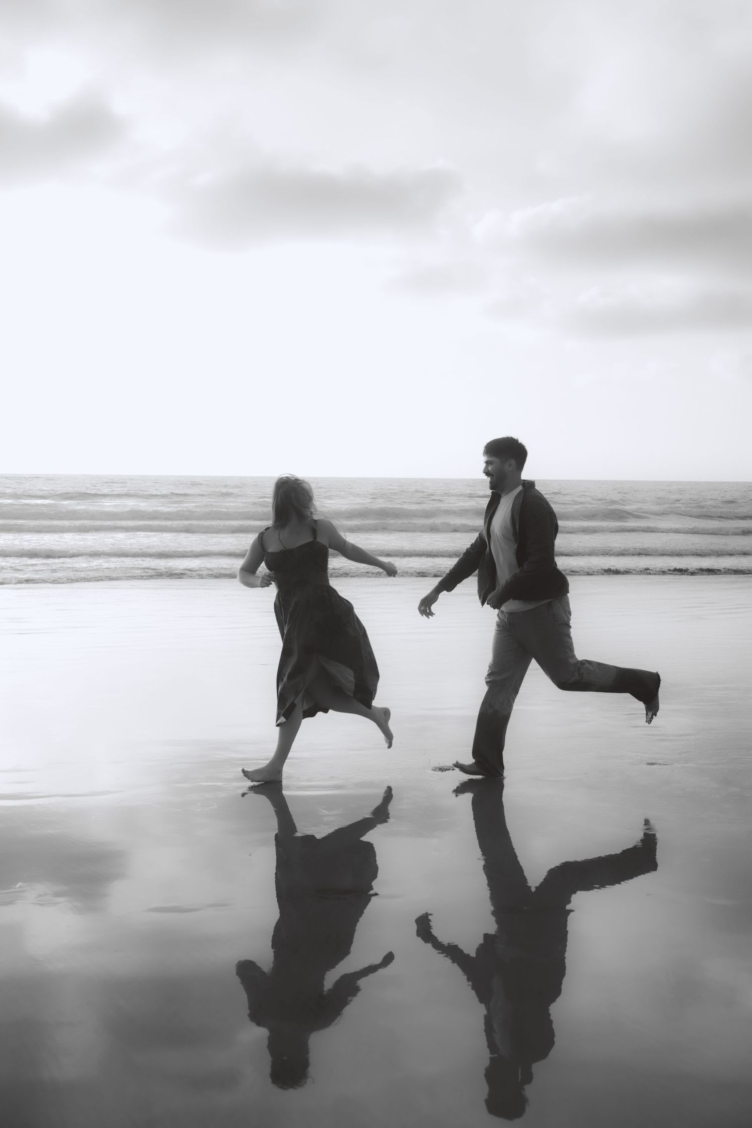 Two silhouettes dance and leap playfully on a reflective beach at sunset creating mirror images in the wet sand.