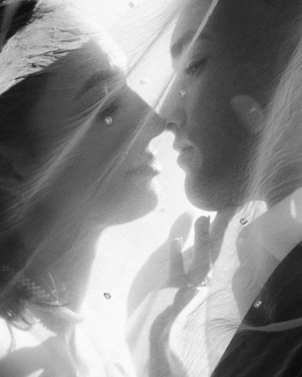 Black and white photo of a bride and groom sharing an intimate moment under a wedding veil.