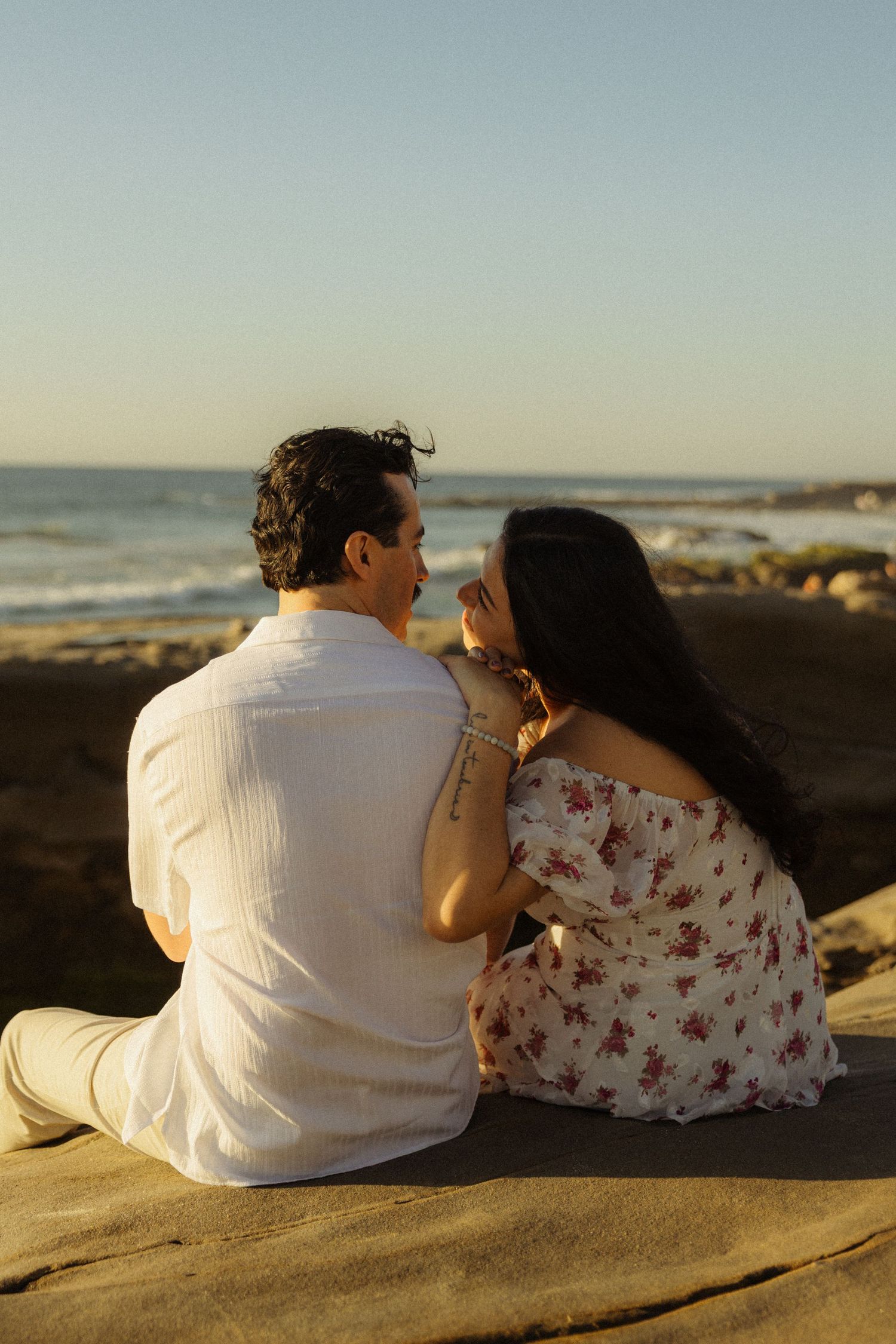 A couple sits together on a sandy beach during golden hour, viewed from behind in a series of romantic poses.