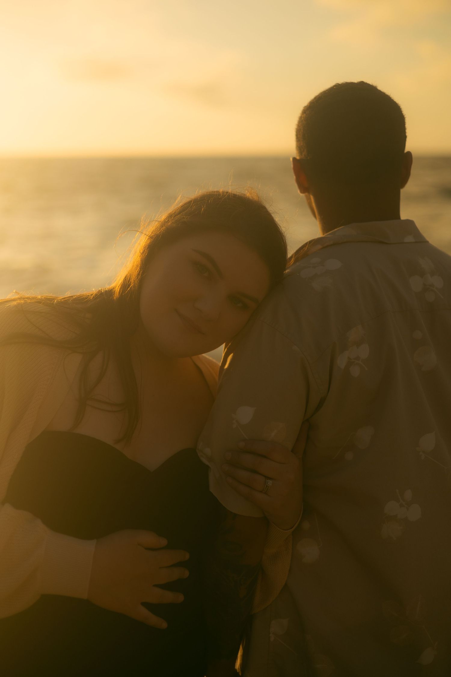 A couple embraces in silhouette against a warm sunset glow over the ocean.