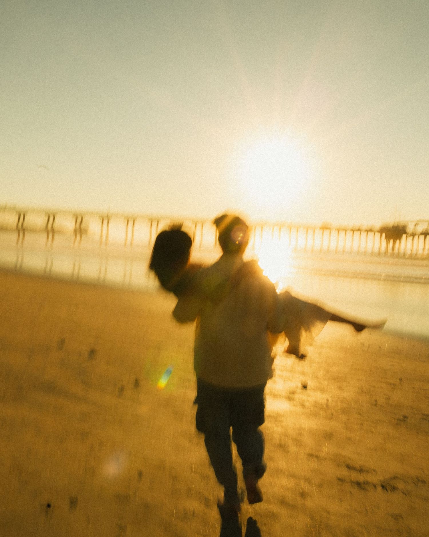Silhouettes of people walking along a beach at sunset with a pier in the distance creating a dreamy atmosphere.