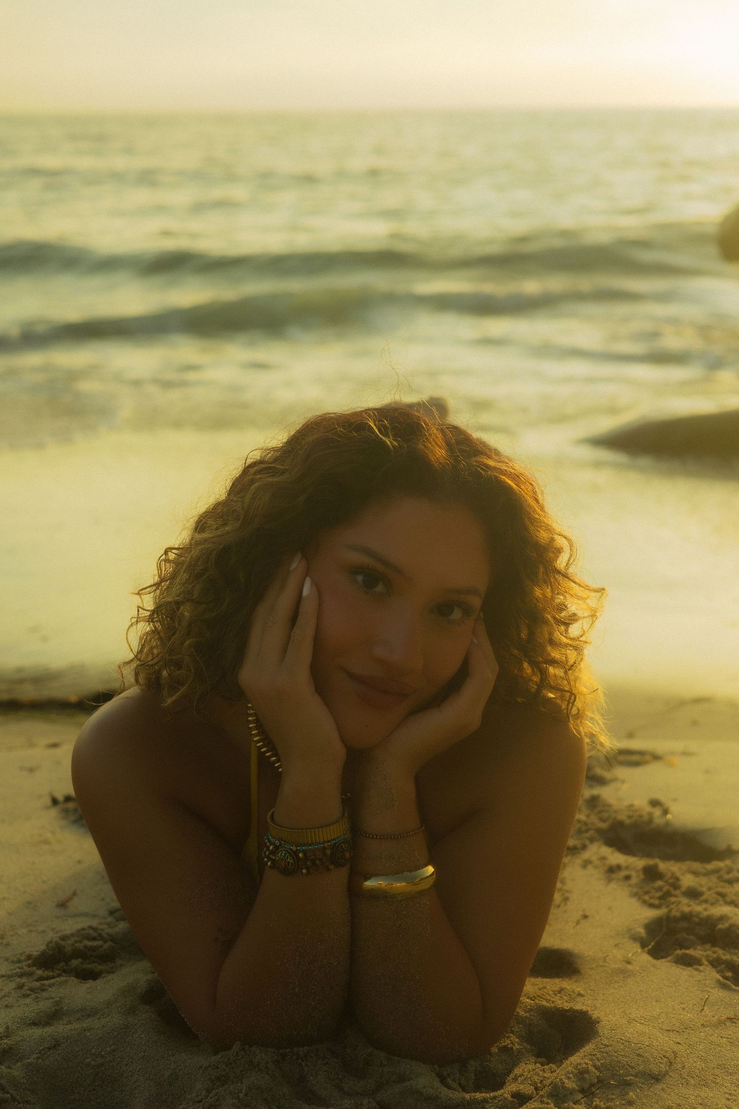 A series of sunset beach portraits showing someone with curly hair lying in the sand at golden hour.