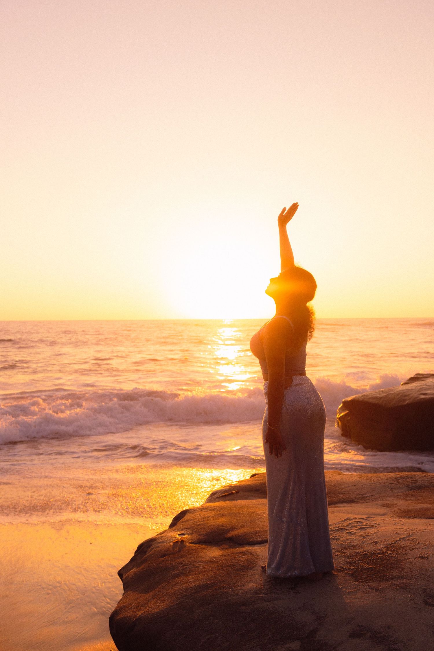 A silhouetted figure stands on rocky cliffs overlooking a misty ocean landscape during a vibrant golden sunset.