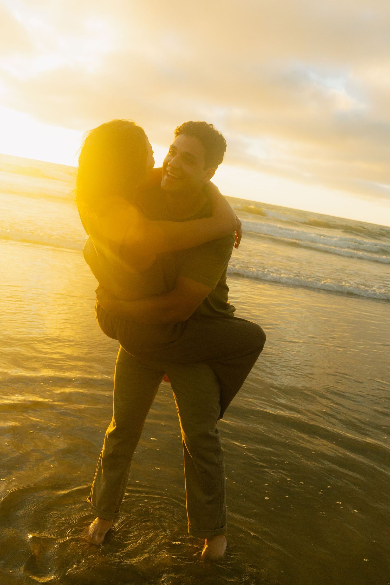 Silhouetted couple embracing on beach at golden sunset with ocean waves in background.