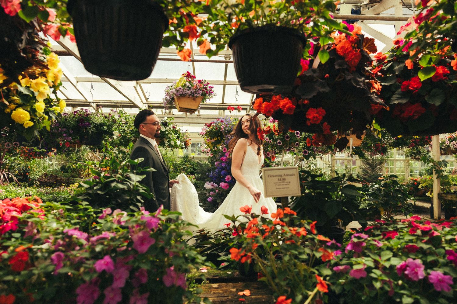 Bride and groom walking among vibrant colorful flowers in a lush greenhouse wedding photo.