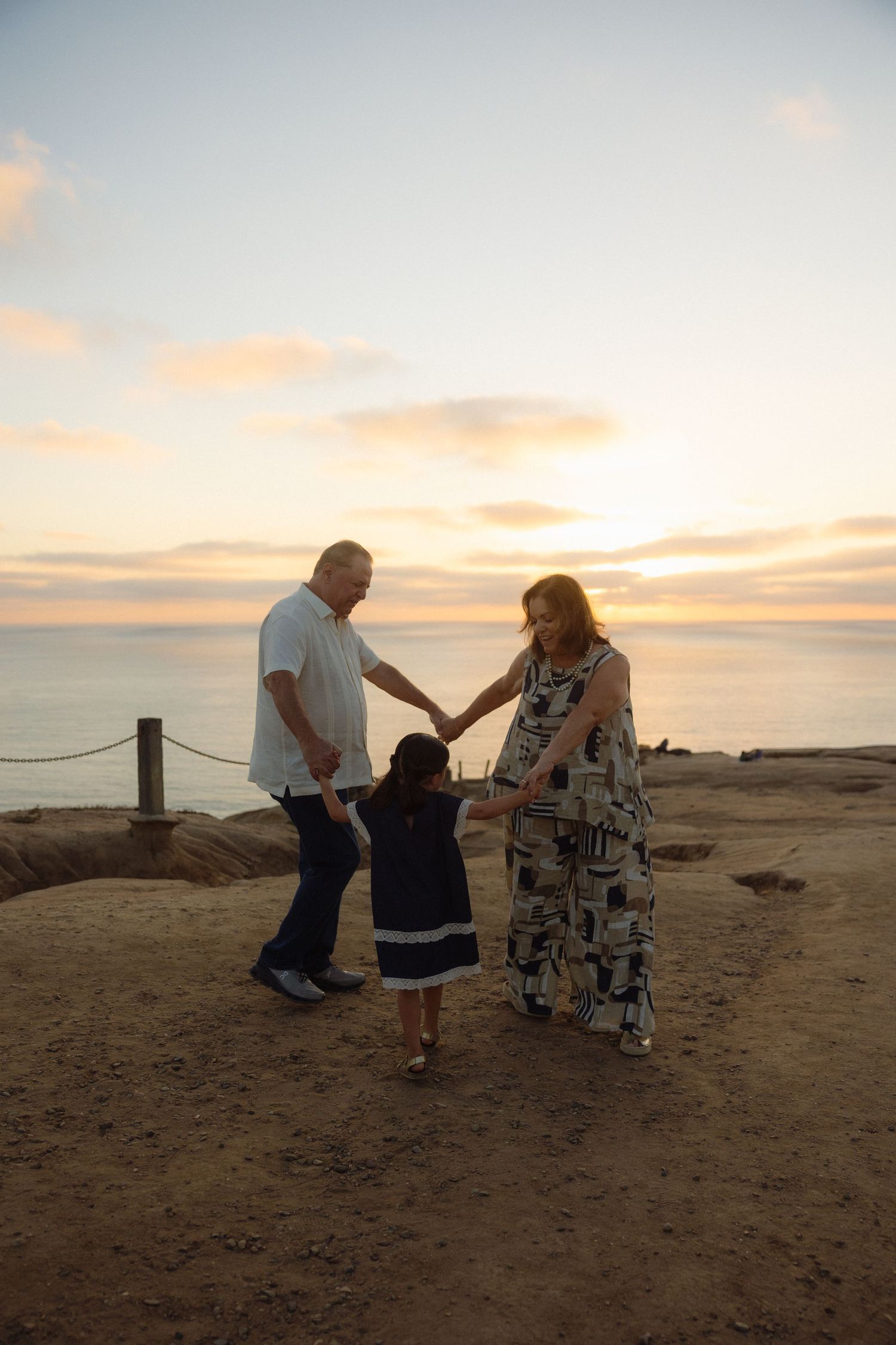 A couple shares a tender moment at sunset on a coastal cliff overlooking the ocean.