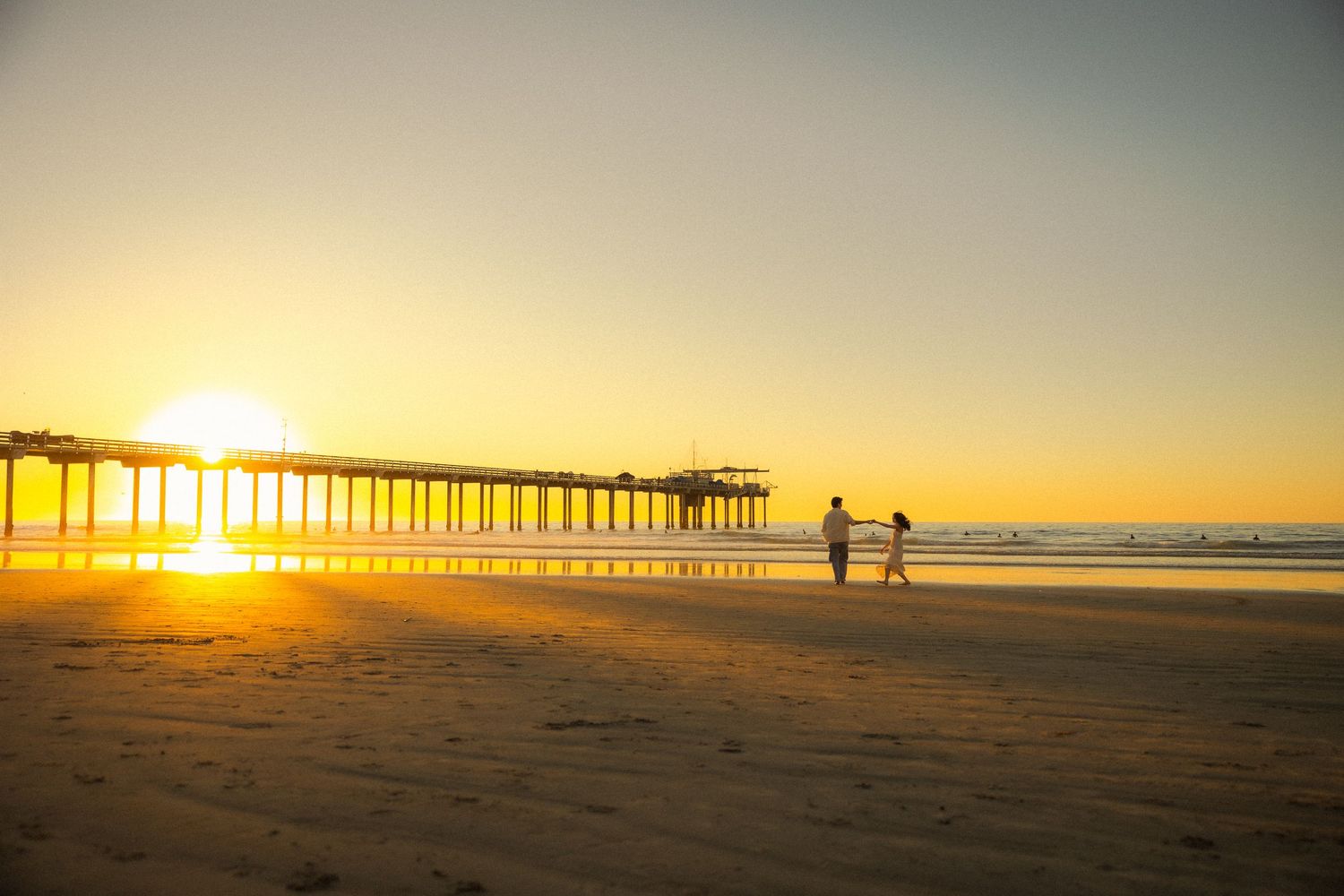Silhouettes of beachgoers walking near a pier during golden sunset at Scripps Beach in La Jolla, California.