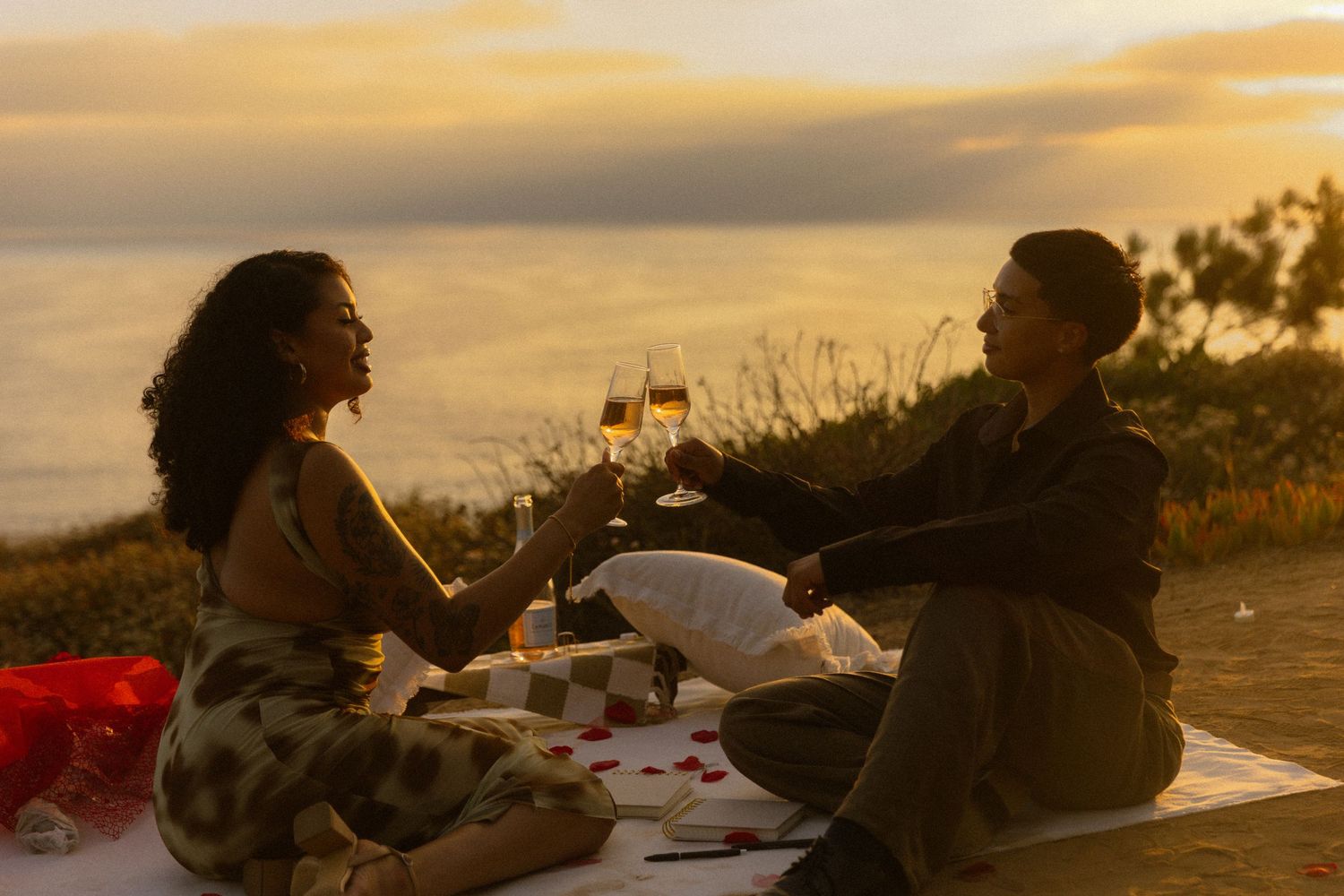 A couple shares wine and conversation during a golden hour picnic overlooking a scenic vista.