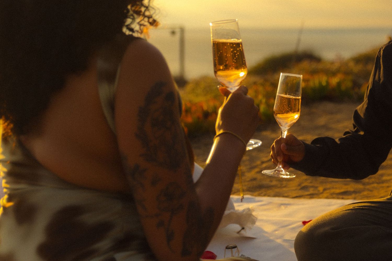 People toasting with wine glasses at sunset during an outdoor gathering with golden light in background.