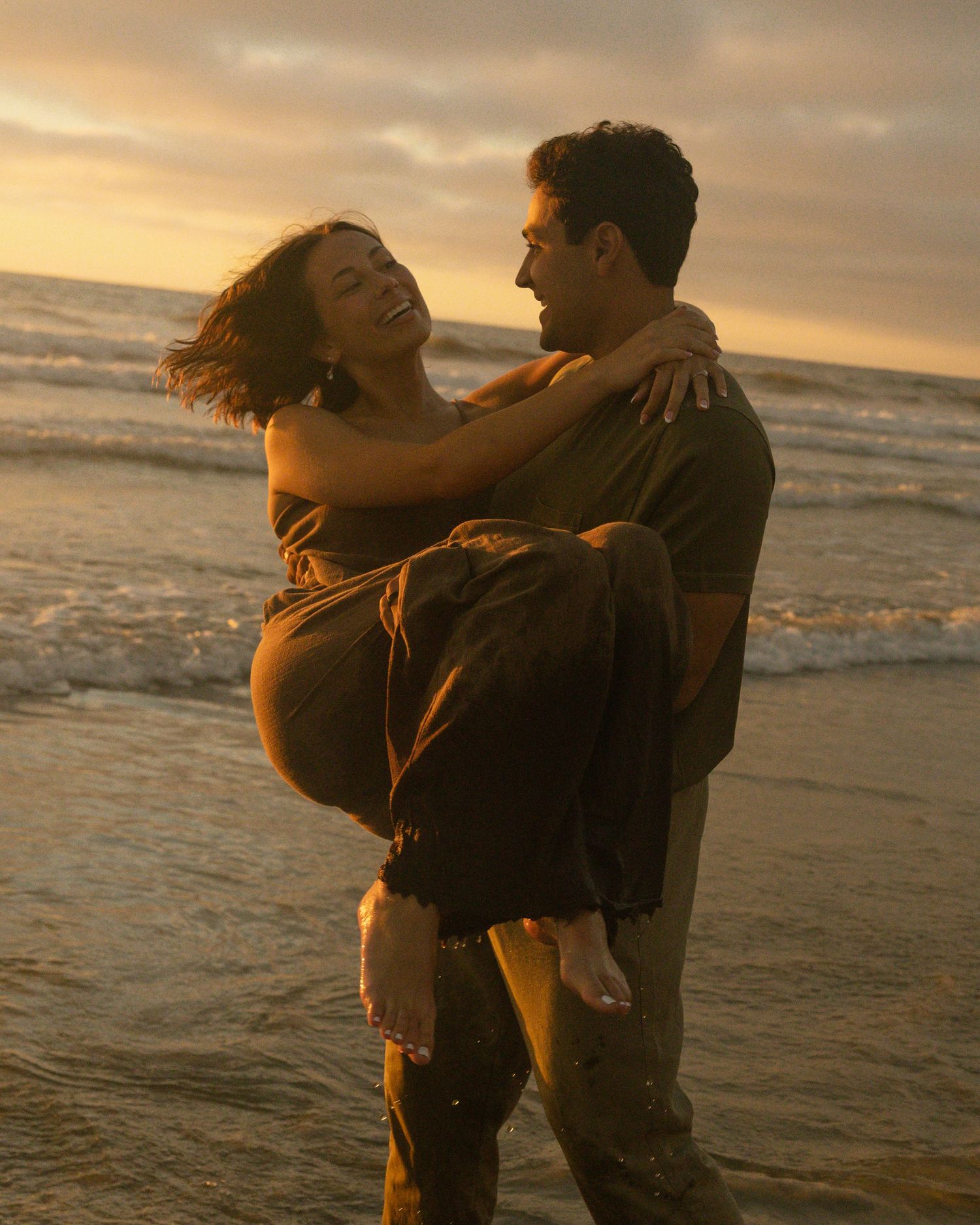 Silhouetted couple embracing on beach at sunset with golden light reflecting off ocean waves.