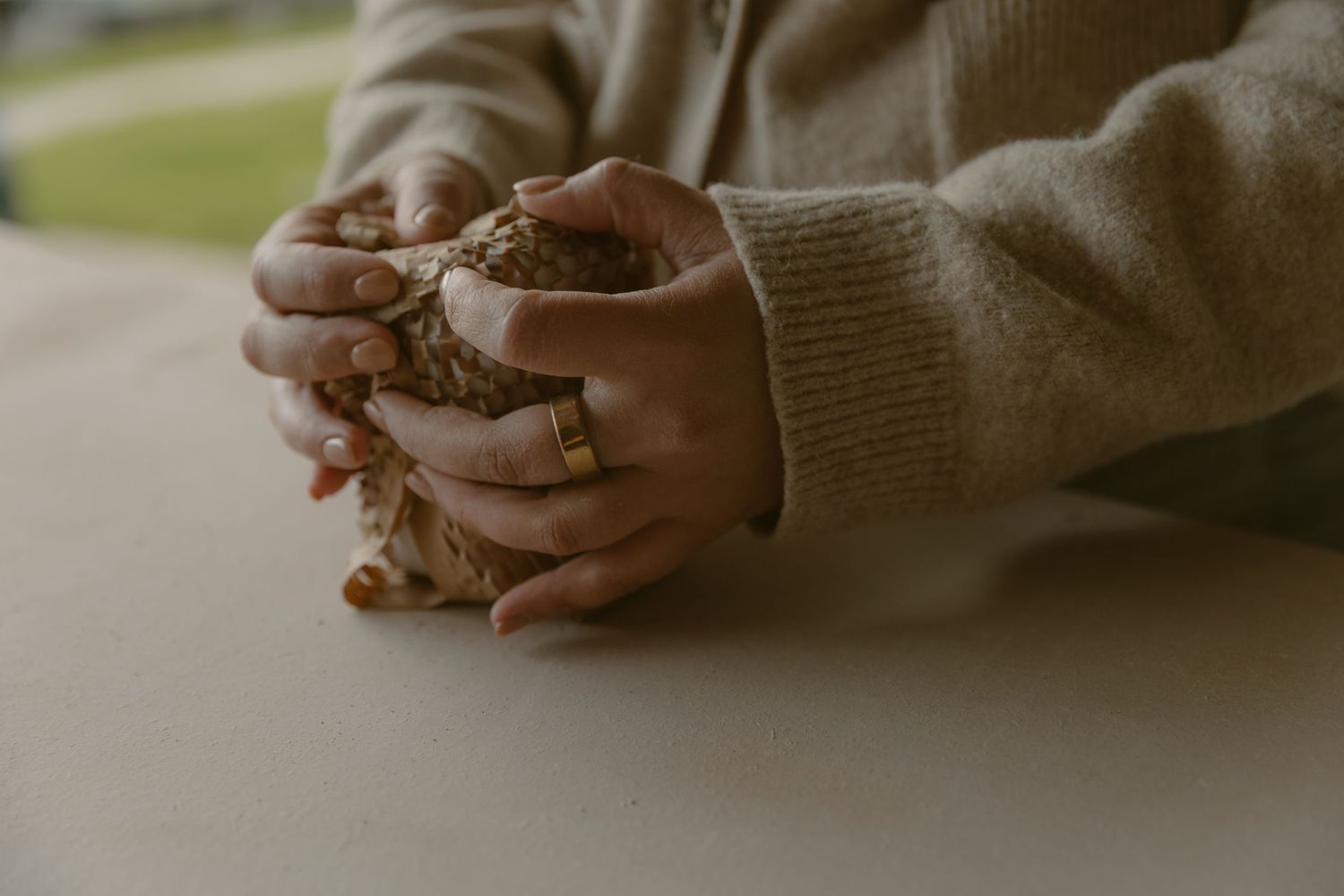 Close-up of hands holding clay pottery in warm knit sweater sleeves.
