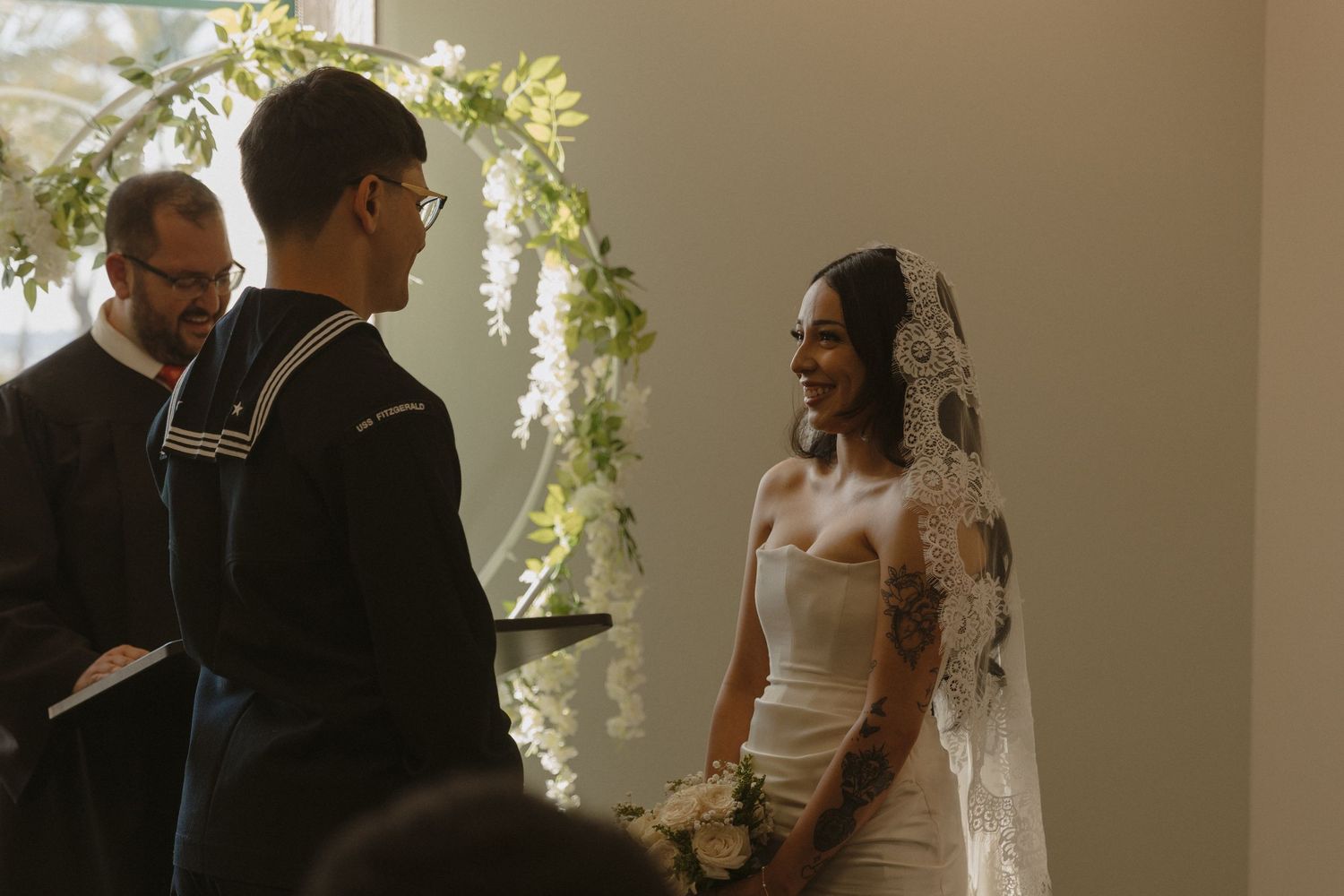 A couple stands at a wedding altar under a floral arch during their ceremony while an officiant performs the service.