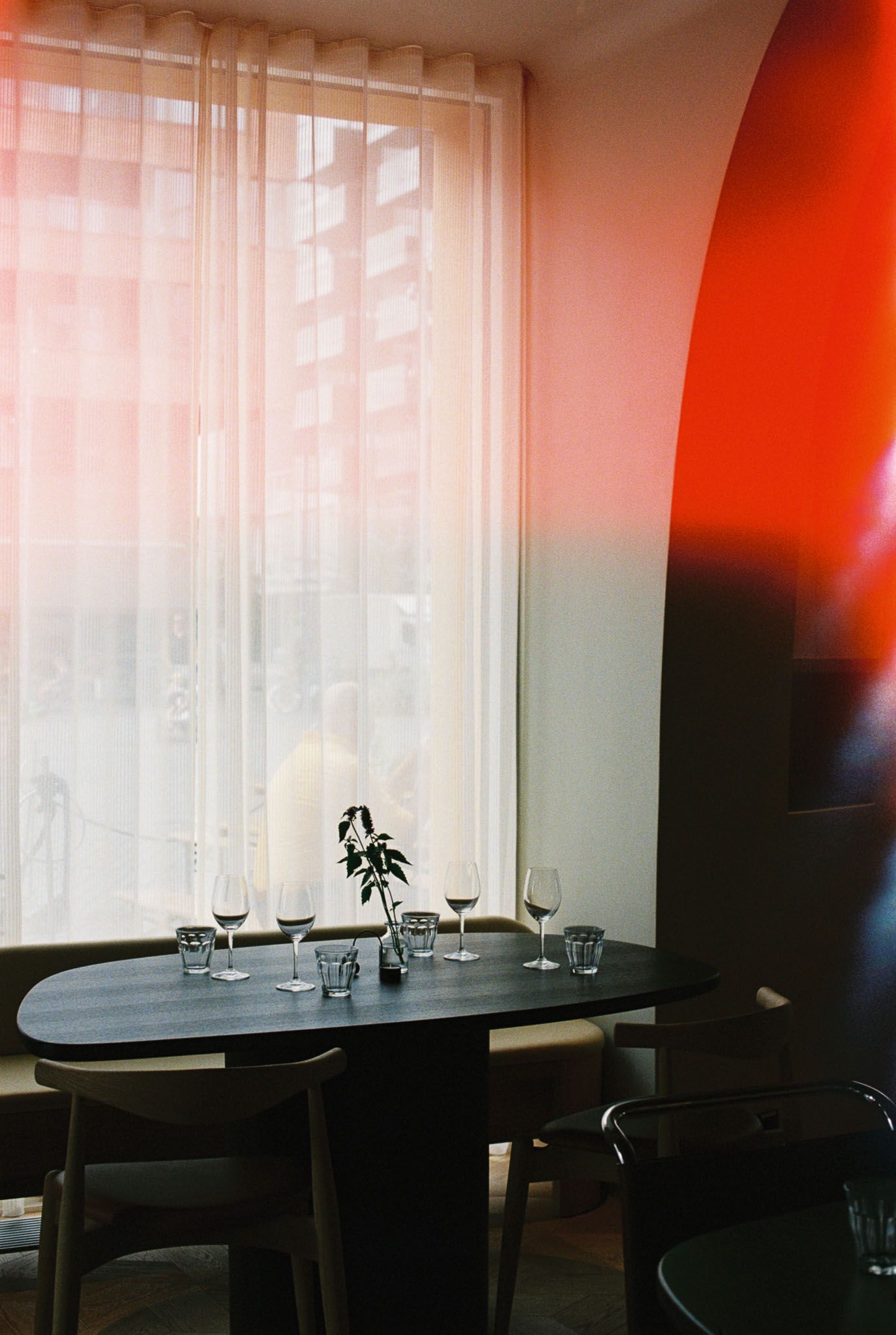 Restaurant table setting with glassware near a window and red gradient wall. Café Platz in Oslo.