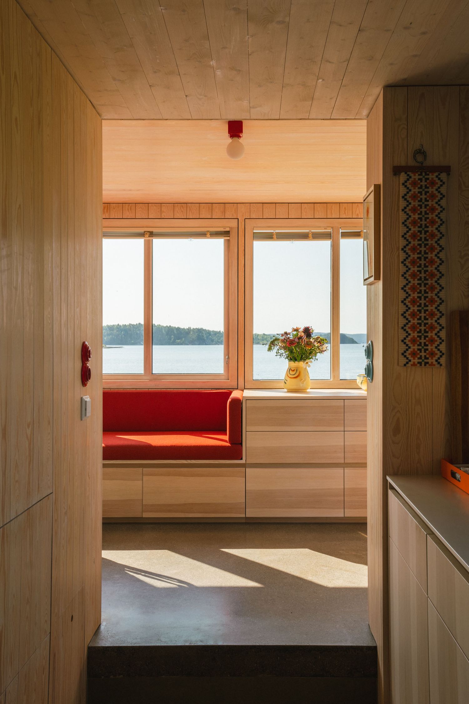 Interior view of a cozy cabin room with red bench seating, wood paneling, and large windows overlooking the Oslo fjord.