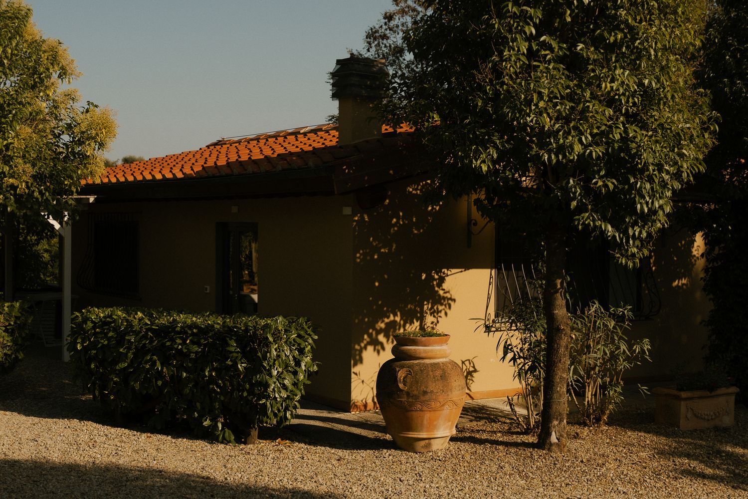 A scenic Mediterranean villa courtyard with terracotta pots and stone pathways surrounded by lush greenery in Toscana.