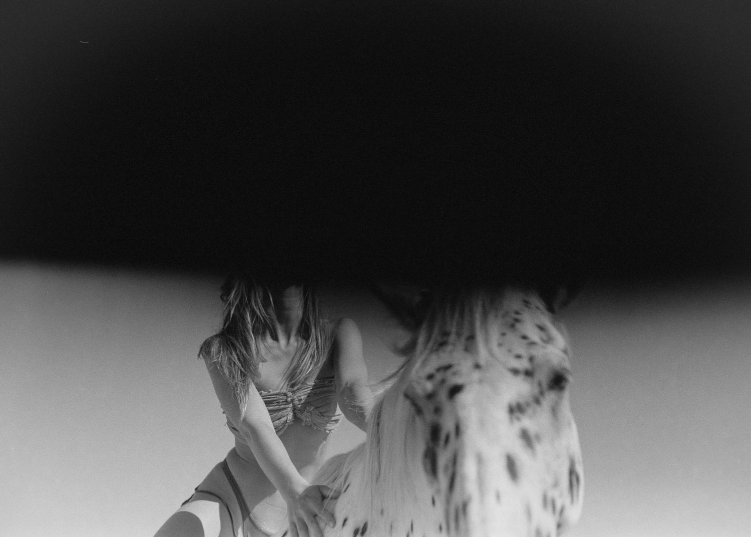 Black and white photo of a person crouching under a large dark shadow with a spotted animal nearby.