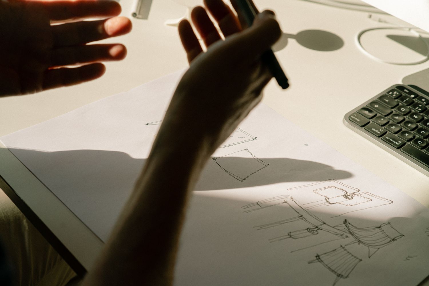 Silhouetted hands casting shadows on a white surface with a keyboard visible in the corner.