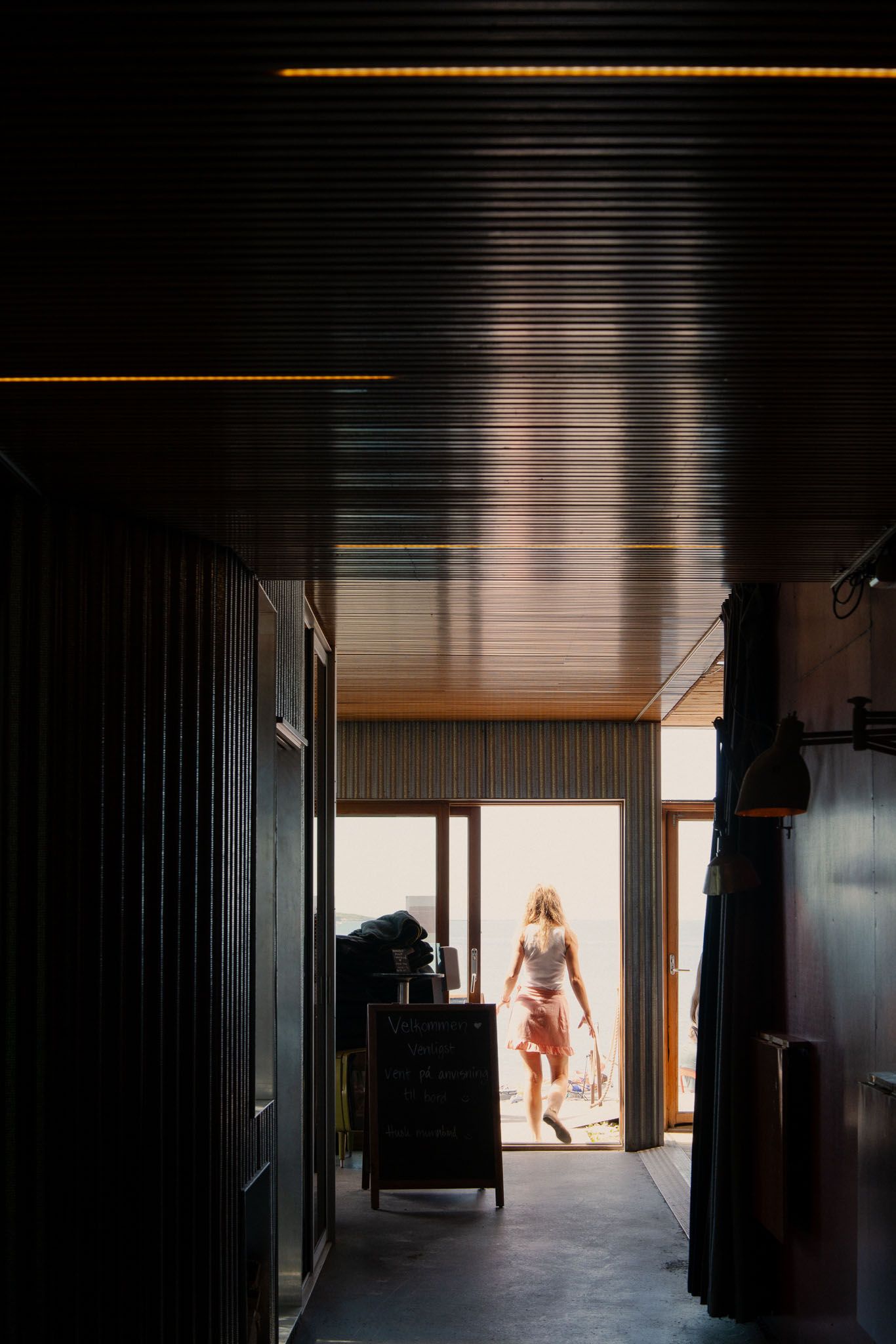 Long dark hallway with dramatic lighting leads to bright doorway at the end.