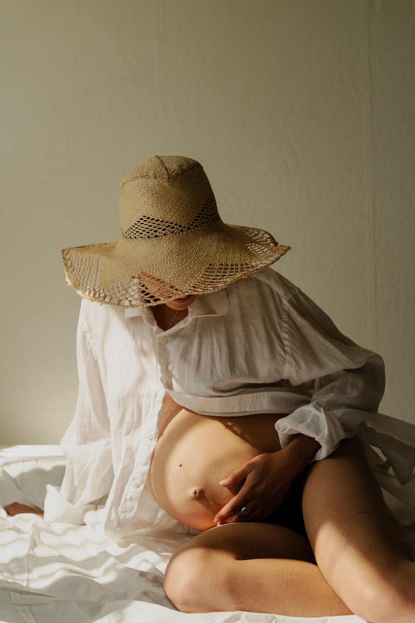 Artistic portrait with straw hat and white clothing against light background.