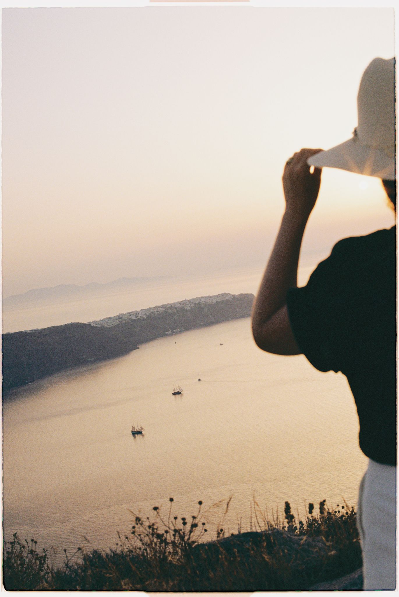 Scenic coastal view at sunset overlooking a curved bay with distant boats on calm waters.
