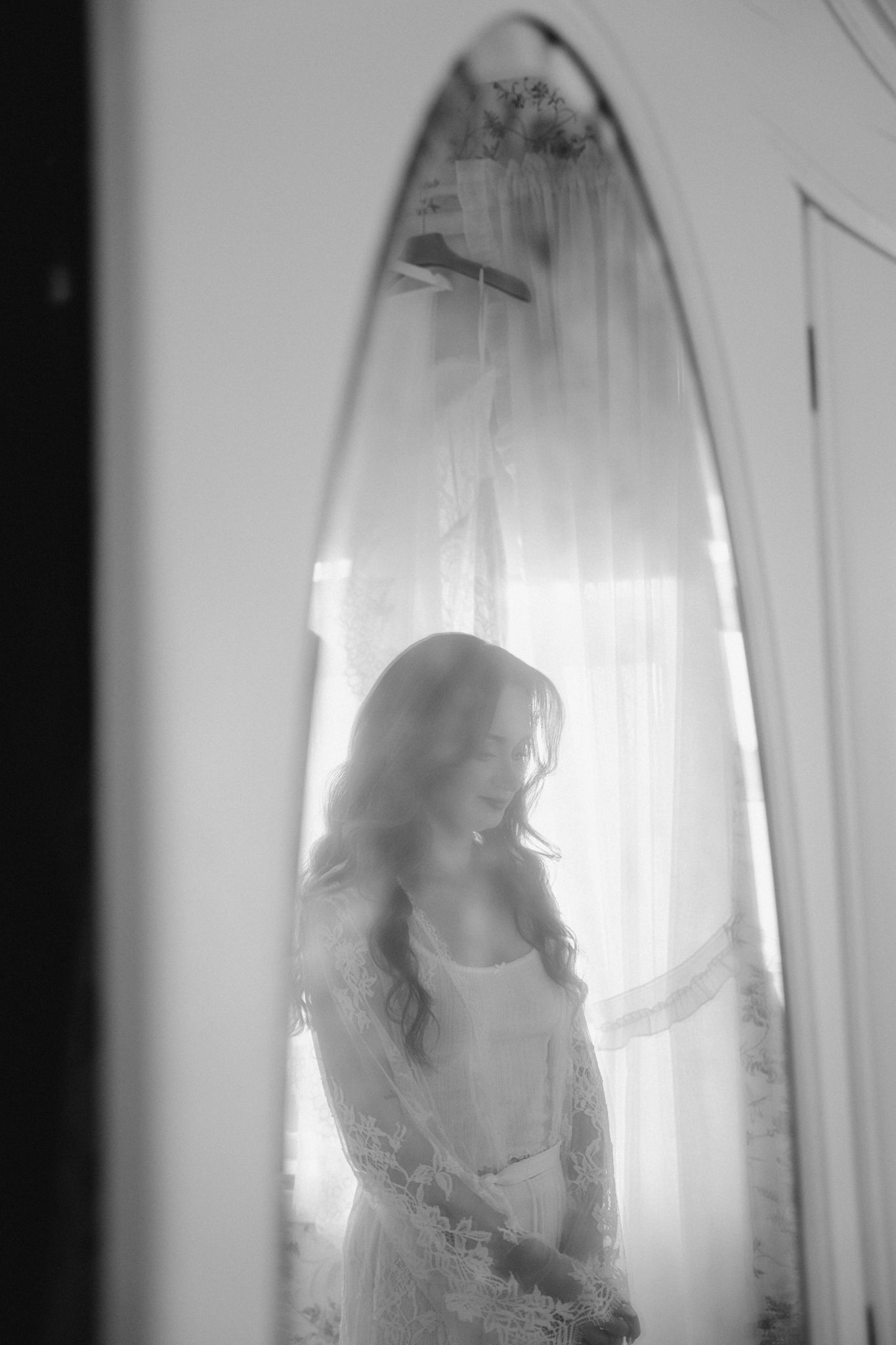A dreamy black and white silhouette behind sheer curtains in soft window light creates an ethereal atmosphere.