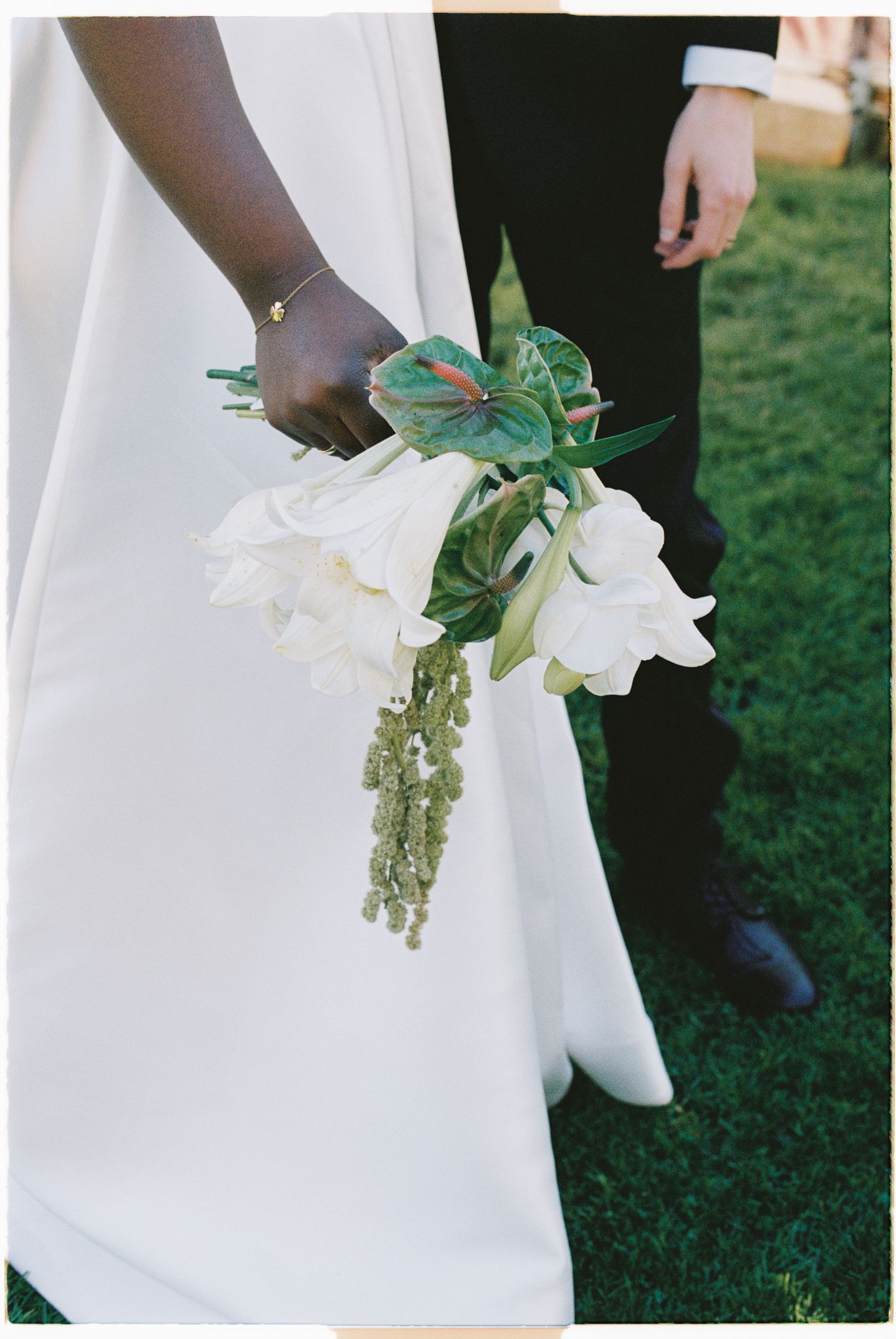 Close-up details of elegant white wedding bouquet with cascading amaranthus against flowing white dress fabric.