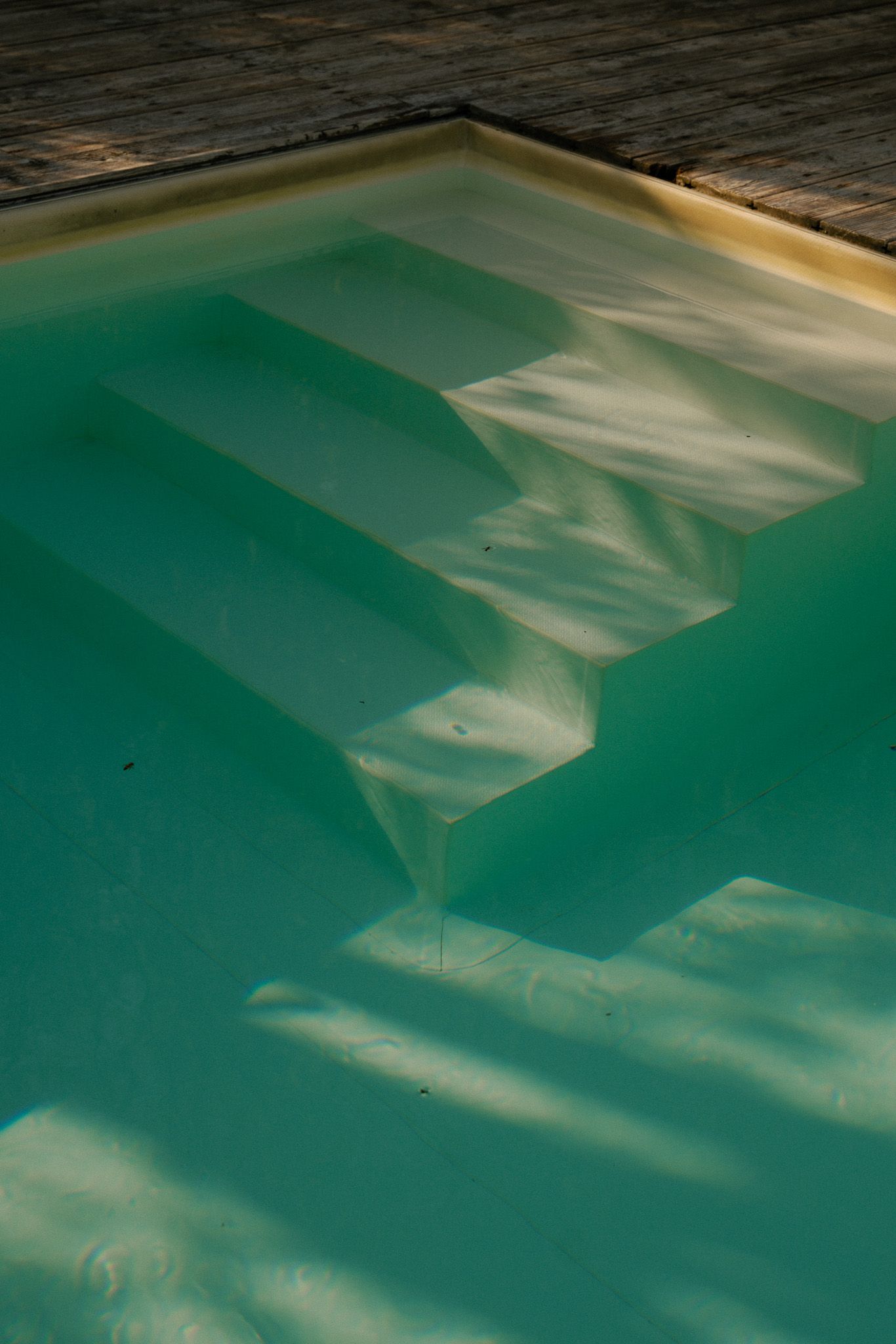 Abstract patterns of light and shadow reflecting on turquoise pool water.