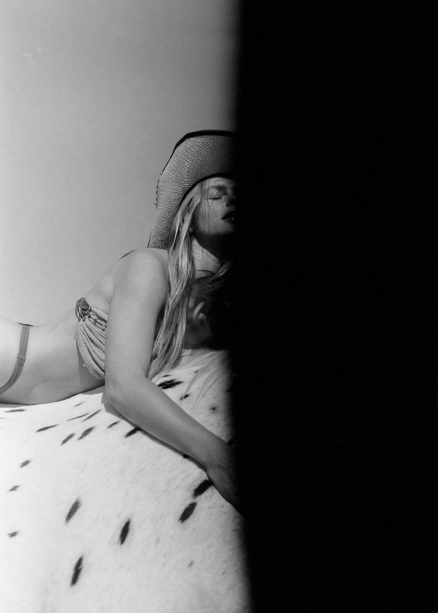 Black and white photo of a woman in a cowboy hat reclining on a spotted surface in soft dramatic lighting.