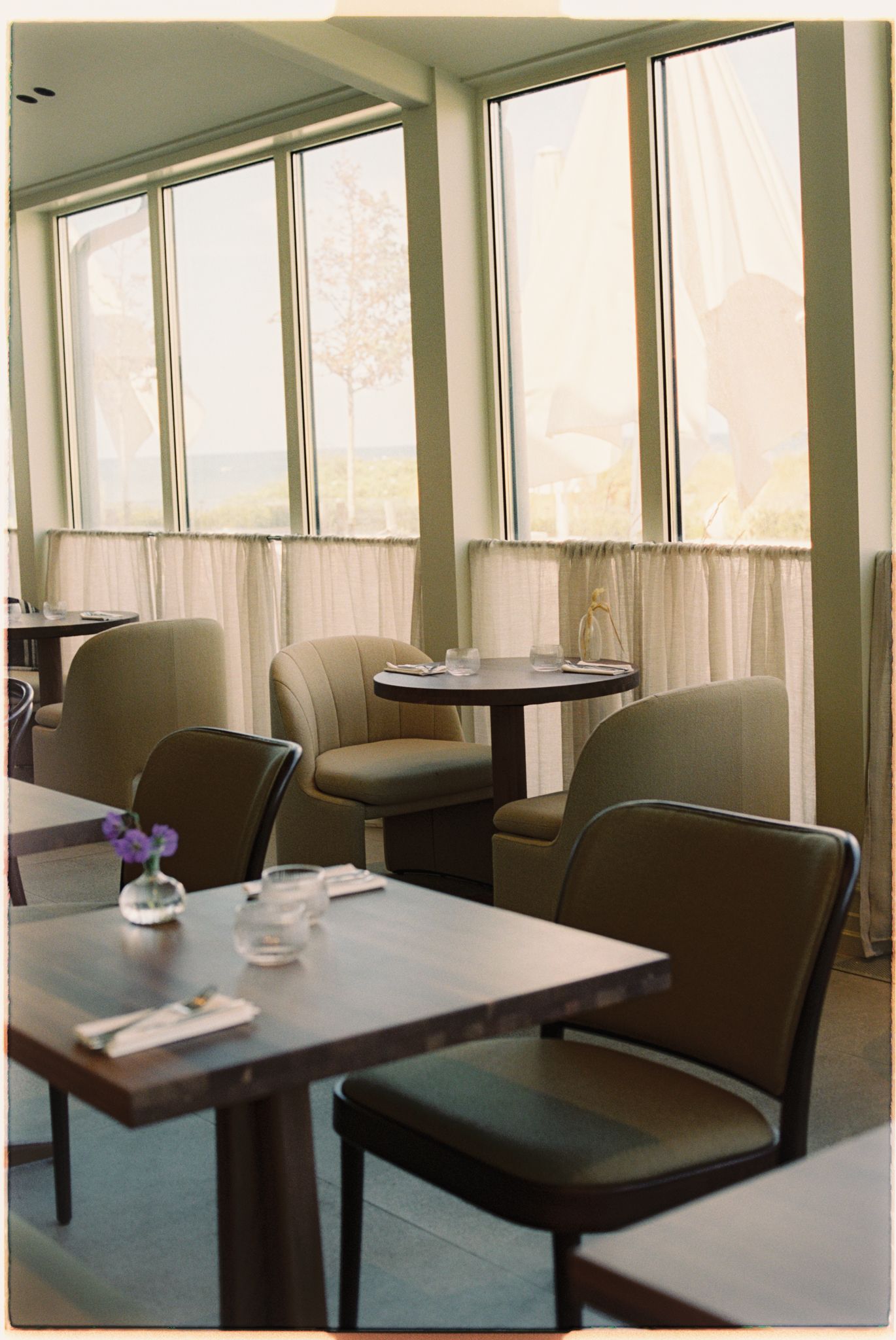 Elegant restaurant dining area with leather chairs, small tables, and floor-to-ceiling windows with sheer curtains.
