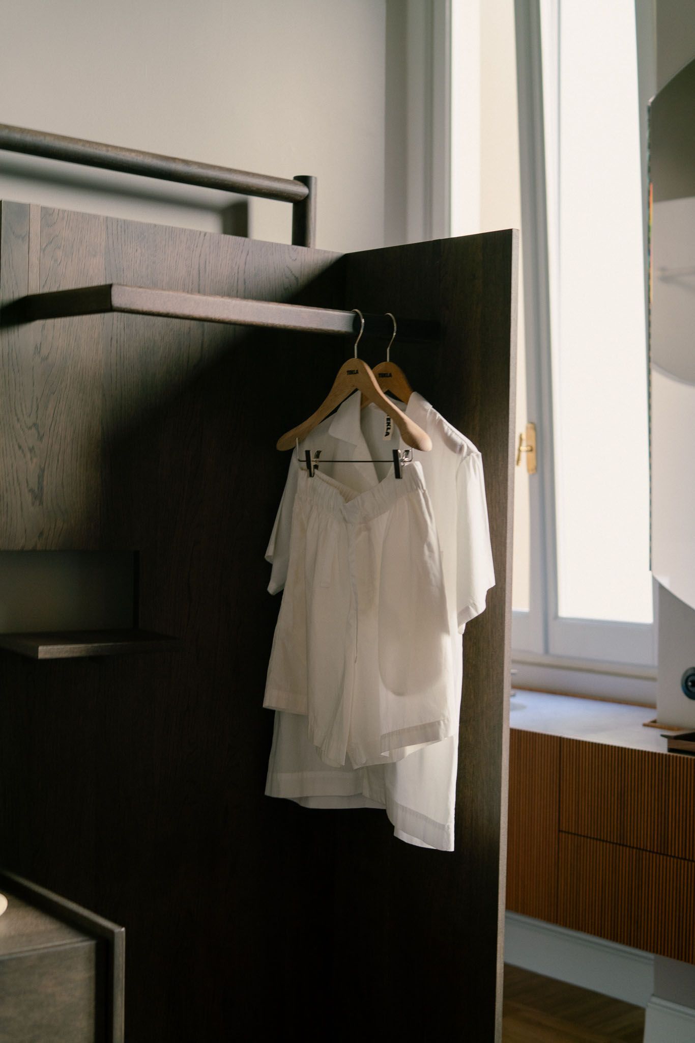 White garments hang on hangers against dark wood paneling in minimalist interior.