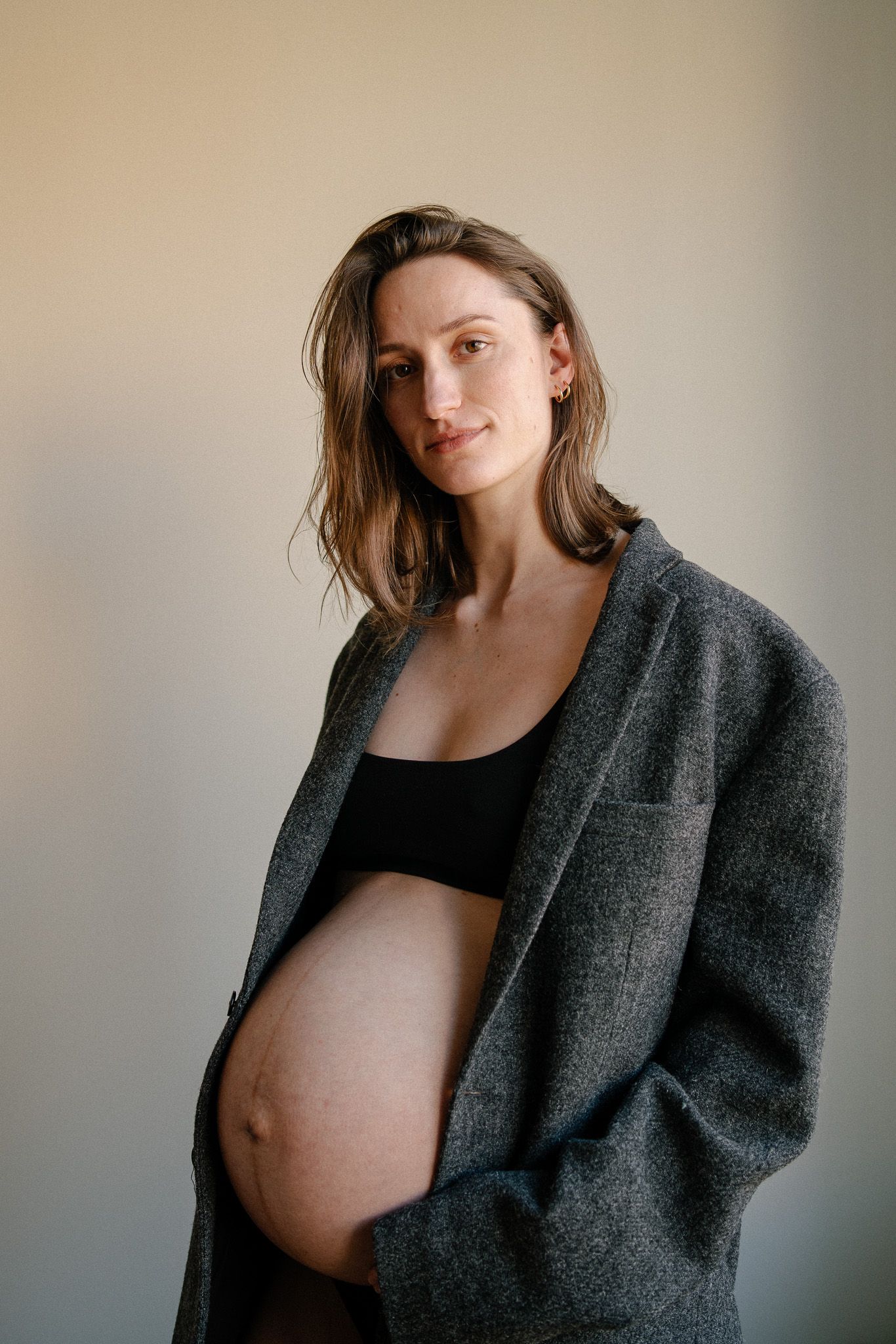 Expectant mother wearing grey coat poses against neutral background.