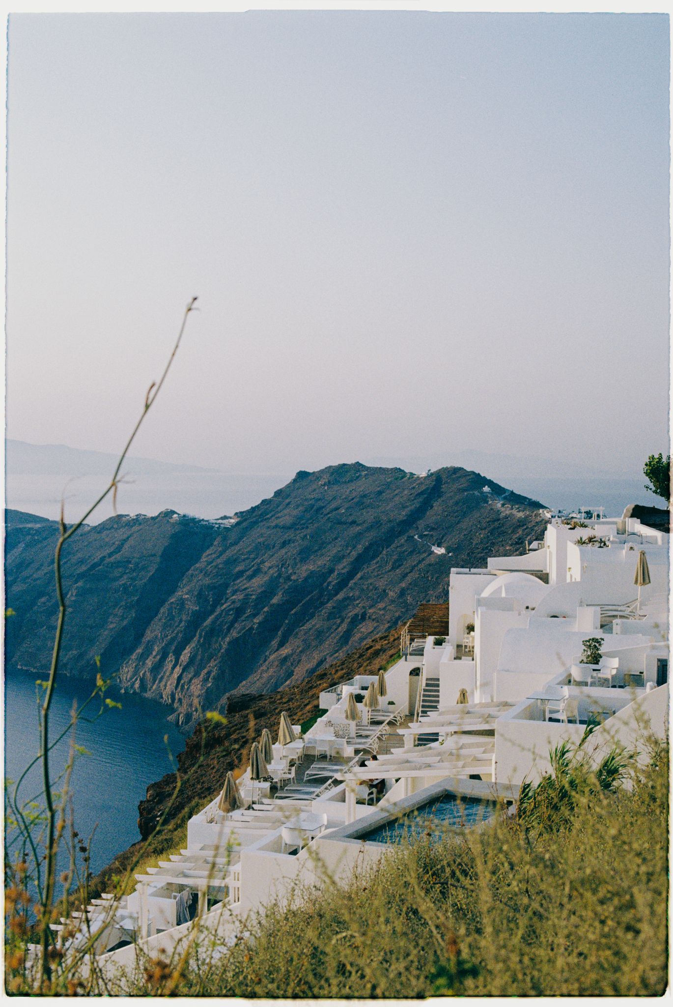 Scenic view of white traditional Greek architecture along cliffside overlooking the deep blue Aegean Sea in Santorini.