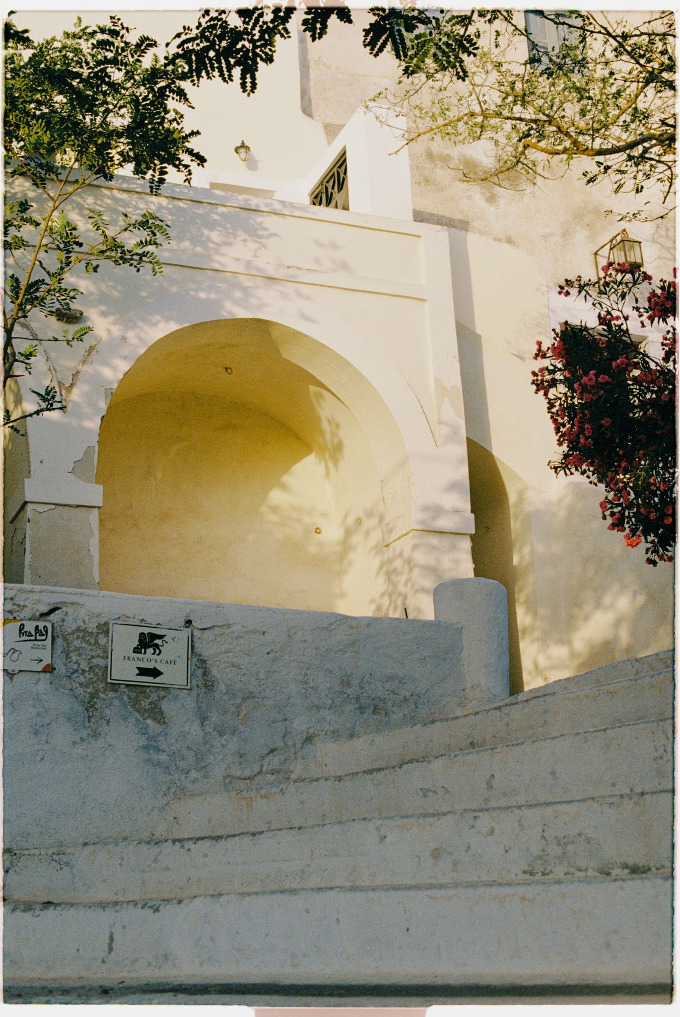 White stucco archway with steps leading up to it, casting soft shadows against a Mediterranean-style building exterior.